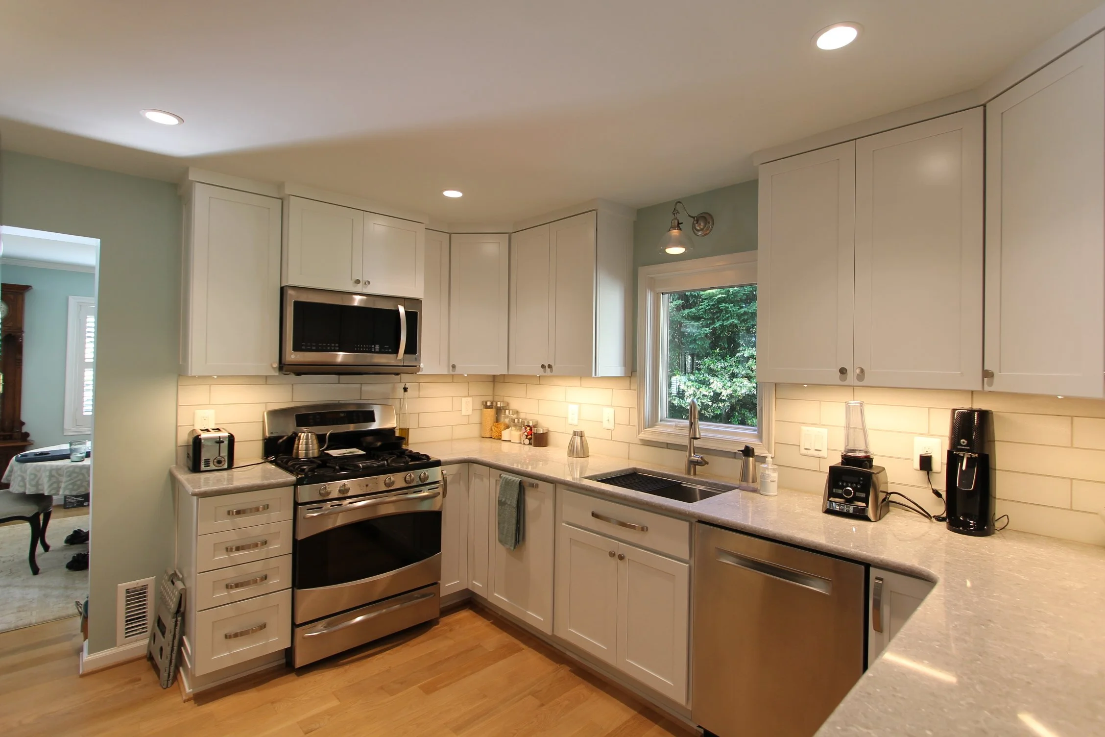 A modern kitchen with white cabinets, stainless steel appliances, a window above the sink, and various small appliances on the counter.