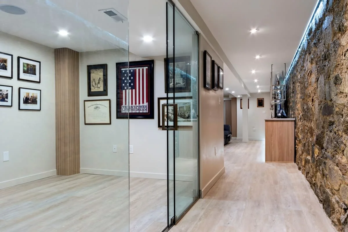 Interior view of a modern home featuring a wall with framed photographs and artwork, a stone accent wall, and a glass partition separating the space.