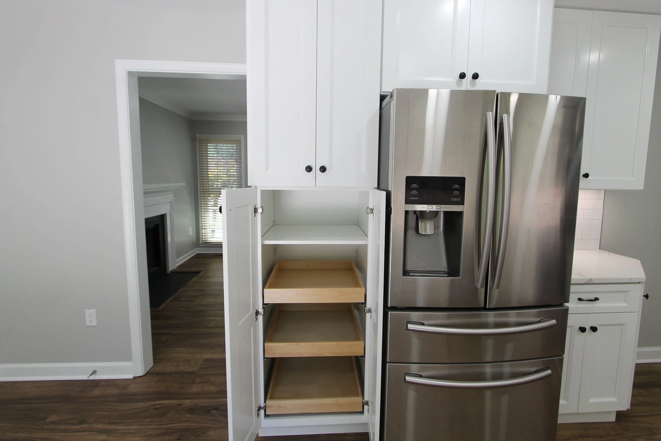 Empty kitchen cabinet with open doors revealing shelves, next to a stainless steel refrigerator.