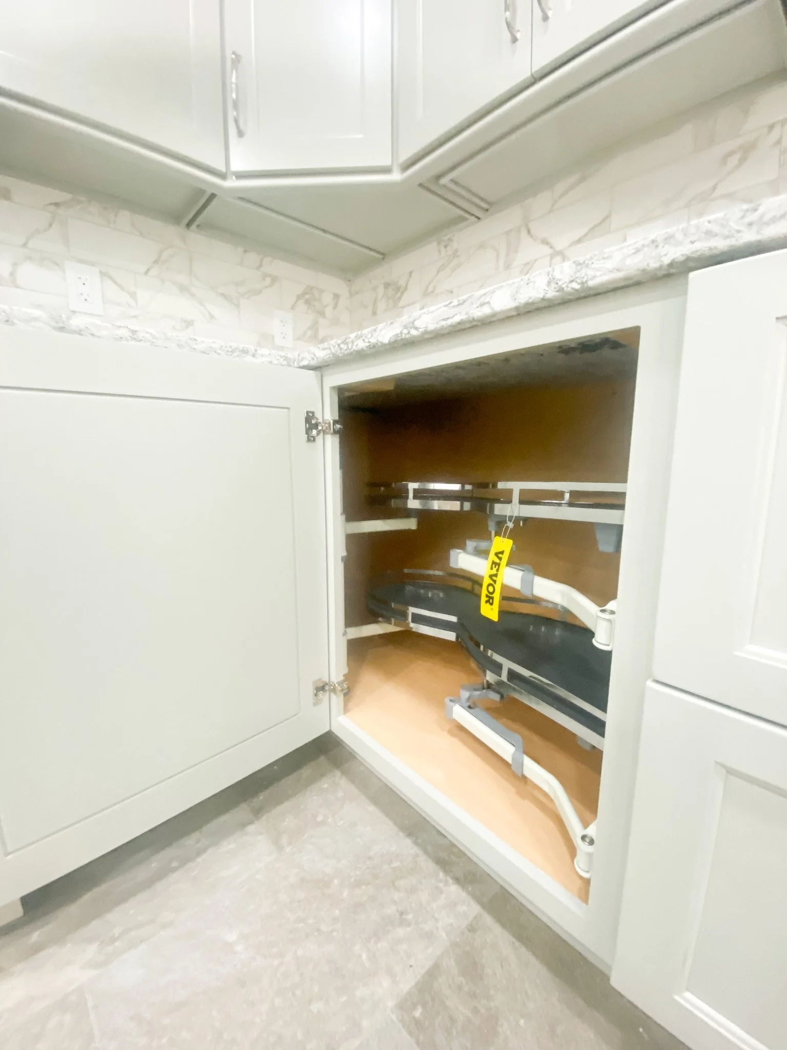 Kitchen cabinet with one door open, revealing a built-in microwave oven with a lift-up door inside a kitchen with white cabinets and a granite countertop.