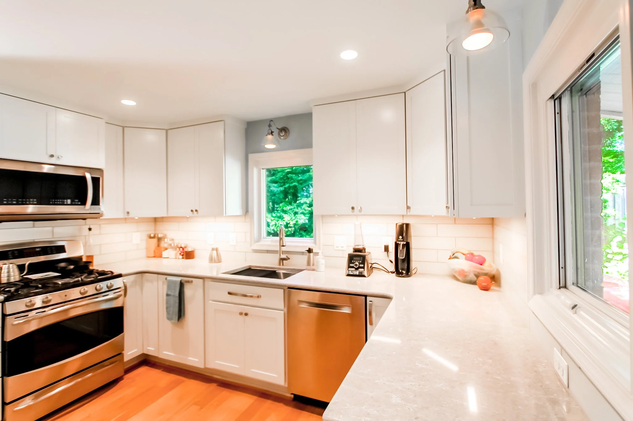 Modern kitchen with white cabinets, stainless steel appliances, a granite countertop, and a window showing green trees outside.