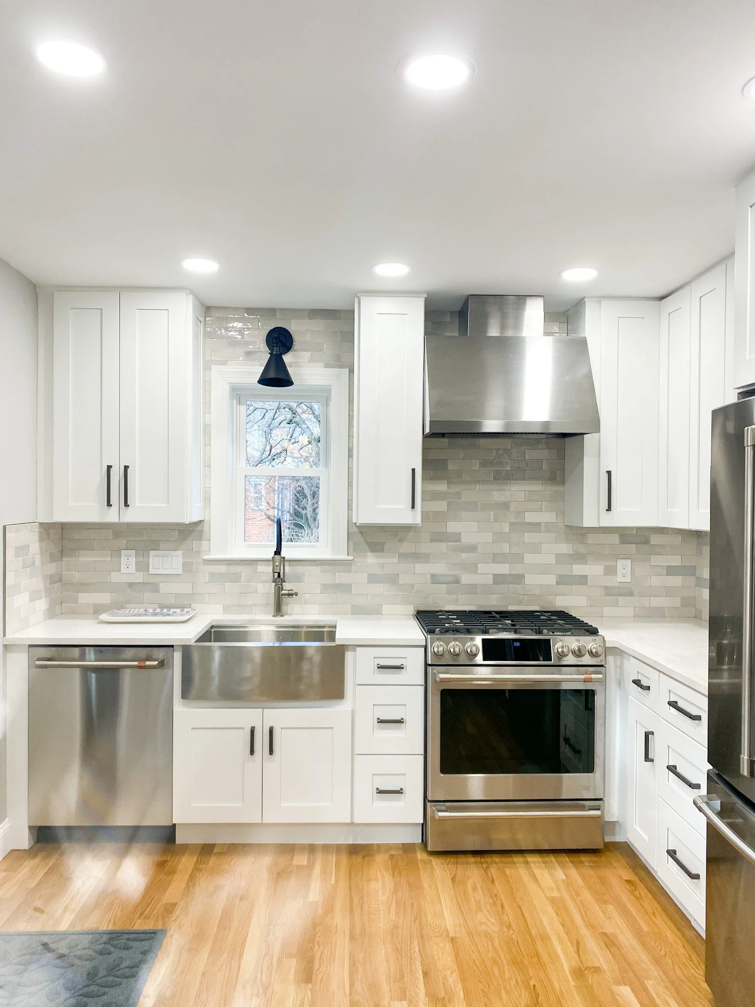 Modern kitchen with white cabinets, stainless steel appliances, a stainless steel farmhouse sink, a window with a view outside, and recessed ceiling lights.