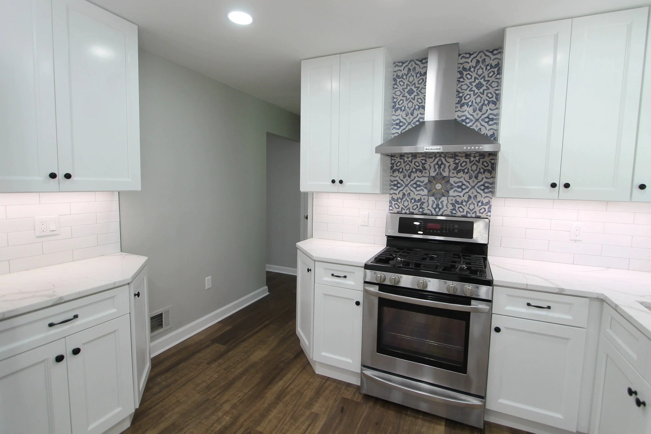 Kitchen with white cabinets, stainless steel oven and range hood, decorative blue and white tile backsplash, and wood flooring.