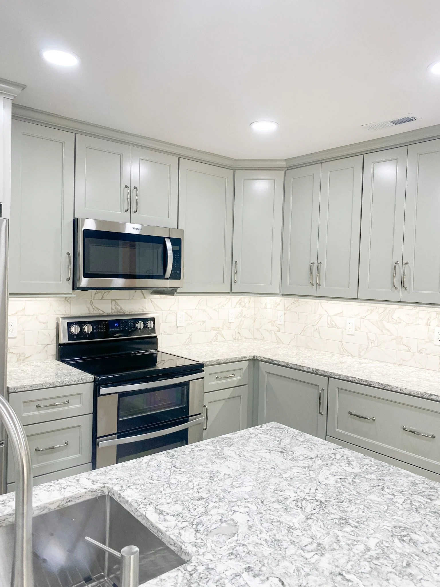 Kitchen with white cabinets, marble countertops, stainless steel microwave, oven, and a visible sink with a faucet.
