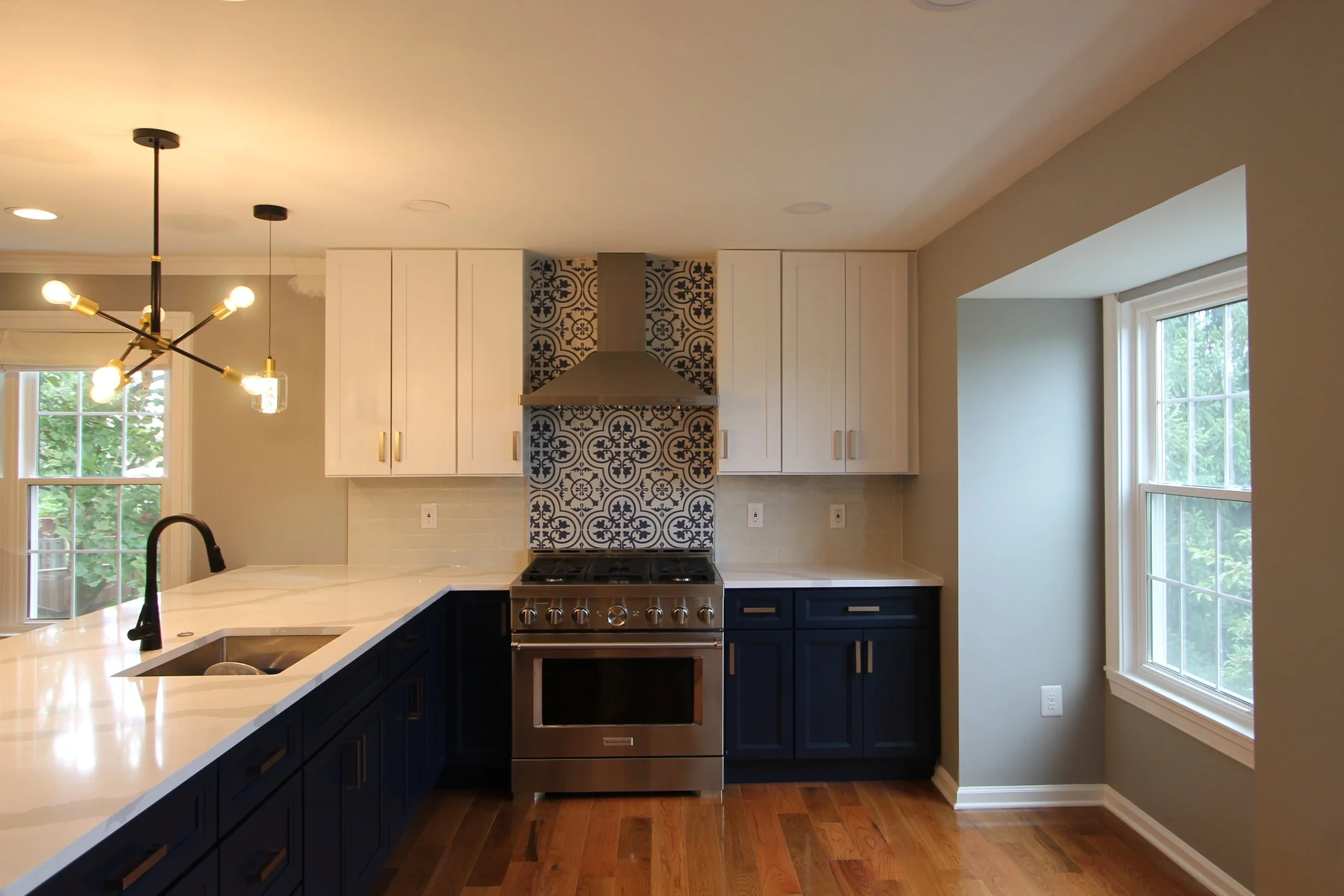 Modern kitchen with white cabinets, a stainless steel stove, a decorative tile backsplash, large windows, and a black and gold chandelier.