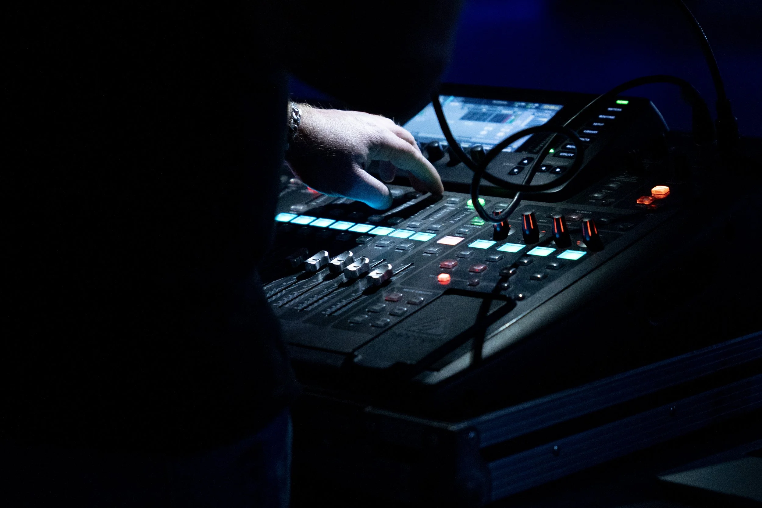 Main d'un DJ appuyant sur des boutons lumineux sur une console de mixage dans l'obscurité.