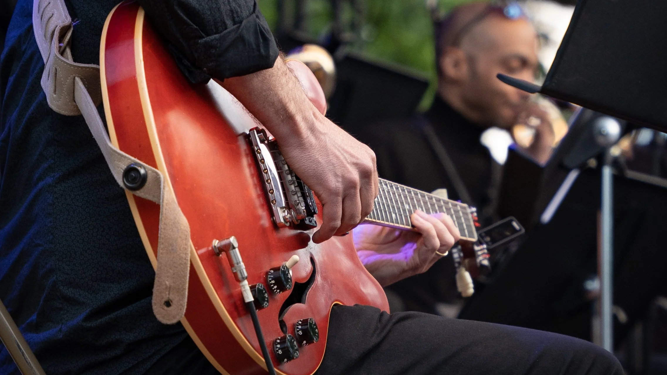 Une personne joue de la guitare électrique lors d'une performance musicale, avec un musicien en arrière-plan, en salle ou lors d'un événement.
