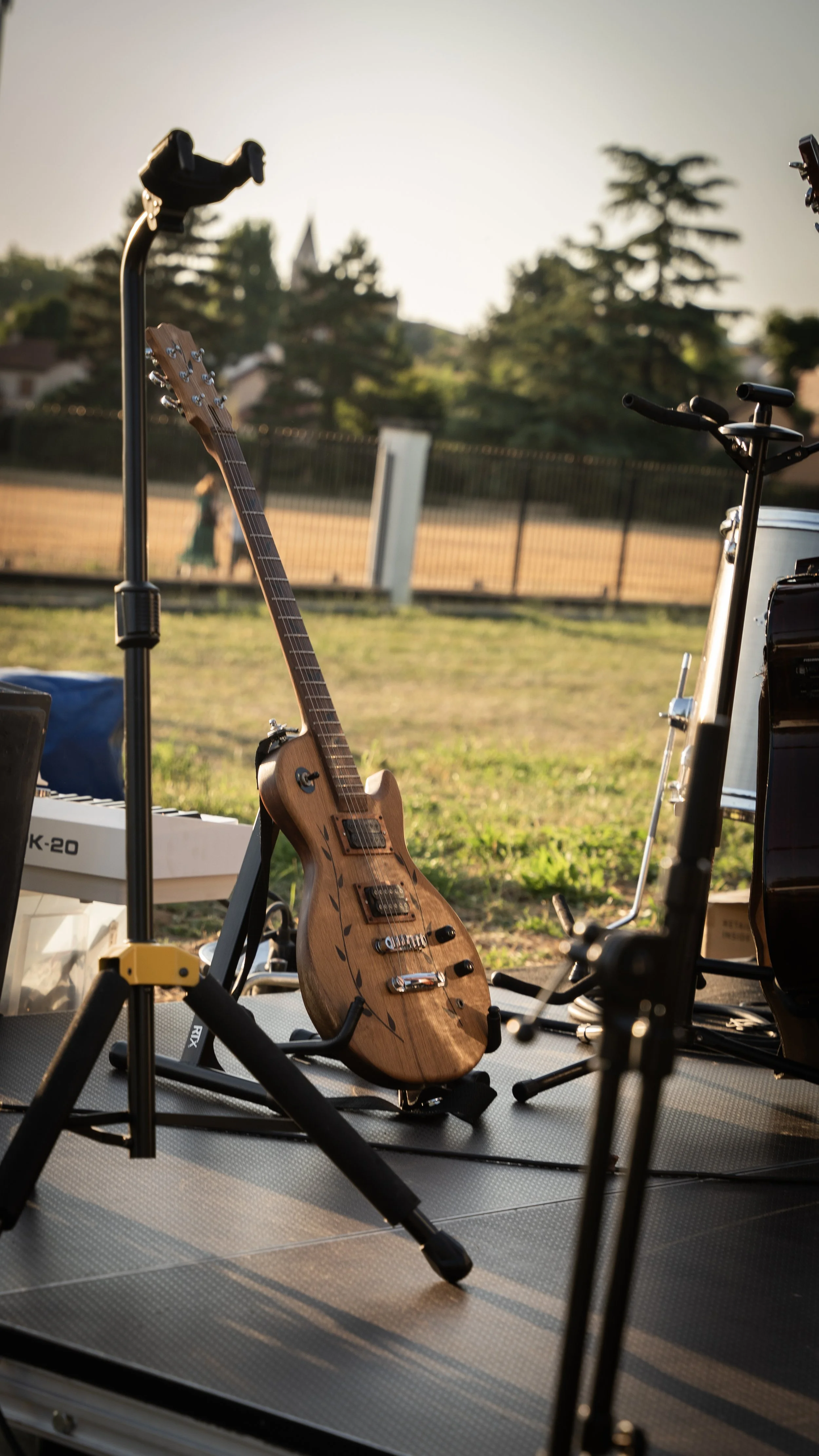 Guitare électrique en bois dans un studio de musique en plein air, avec autres équipements musicaux autour, en fin d'après-midi.