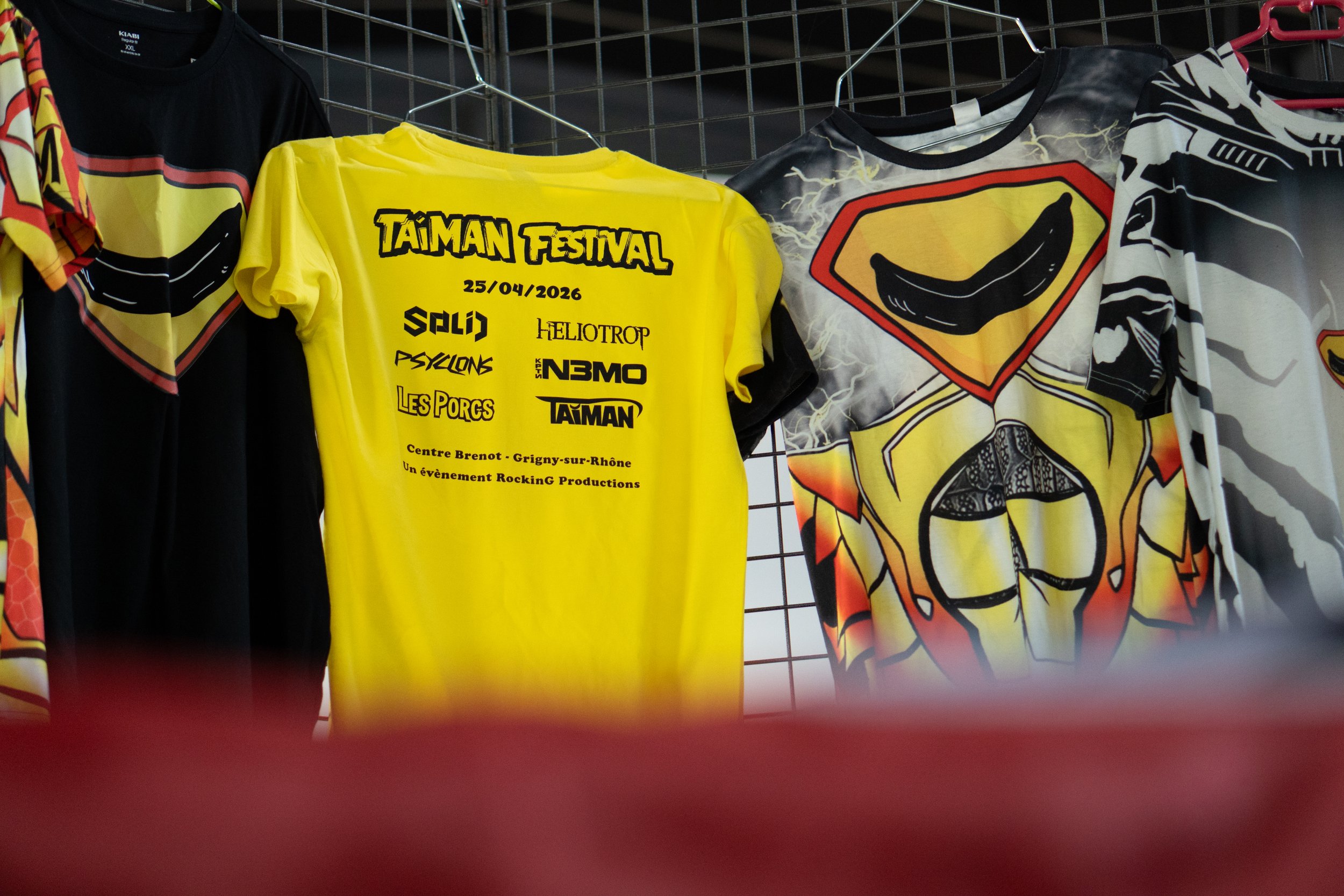 Différents t-shirts aux motifs colorés et logos, suspendus sur une grille dans un magasin.
