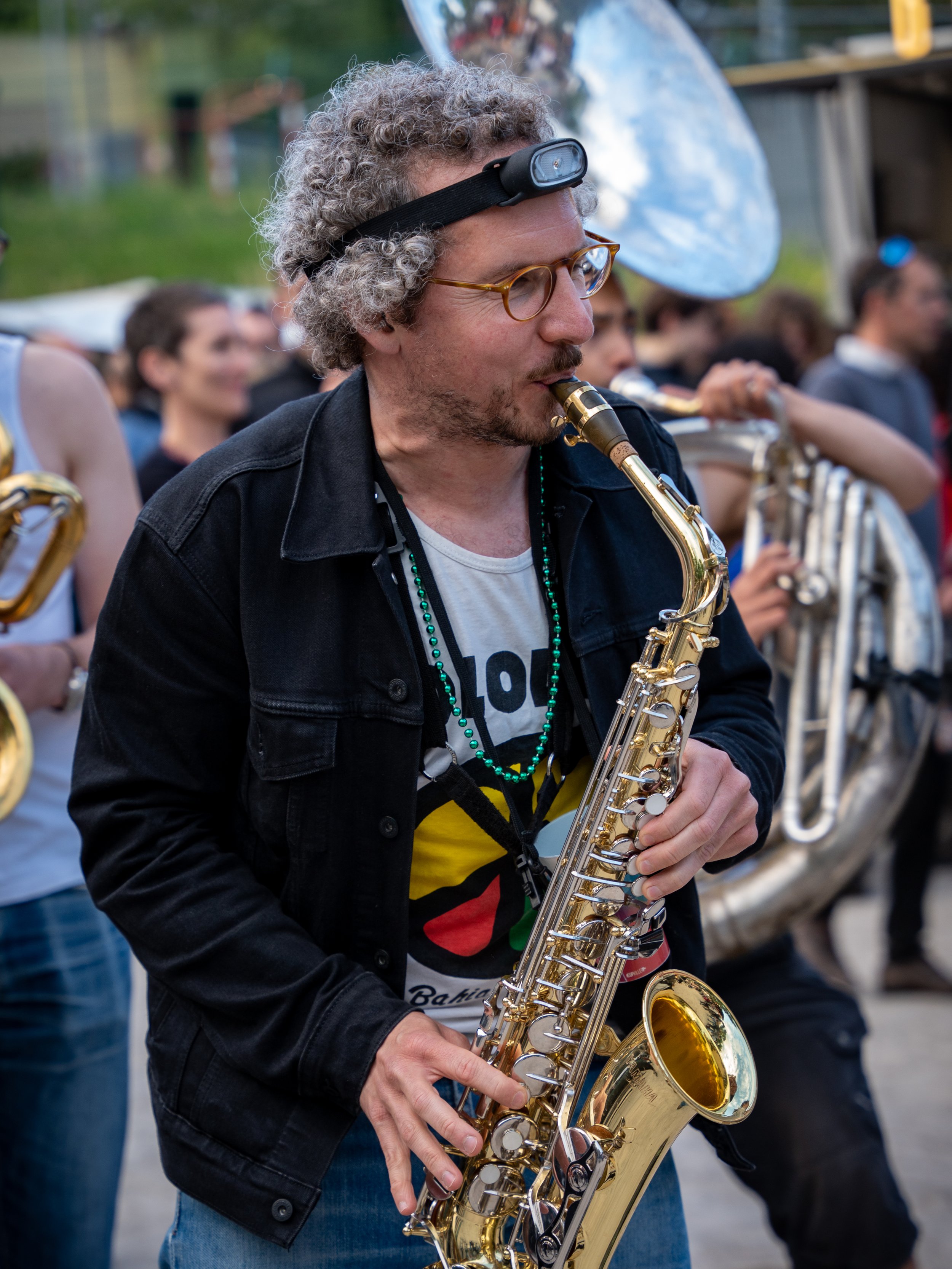 Un homme joue du saxophone lors d'un événement en plein air, entouré d'autres musiciens.