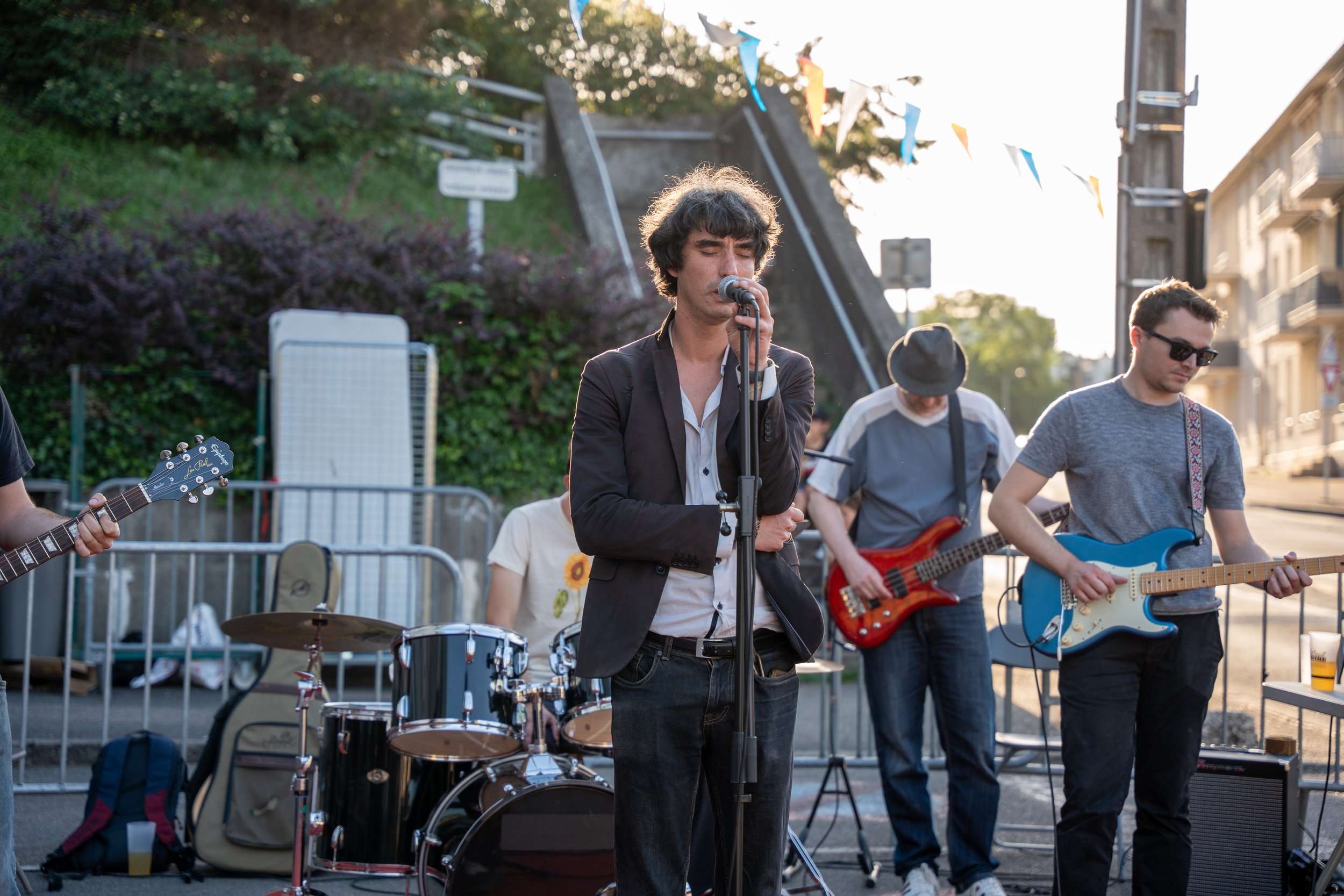 Un groupe de musiciens en train de jouer en plein air, avec un chanteur au centre et des instrumentistes à ses côtés, lors d'une performance en soirée.