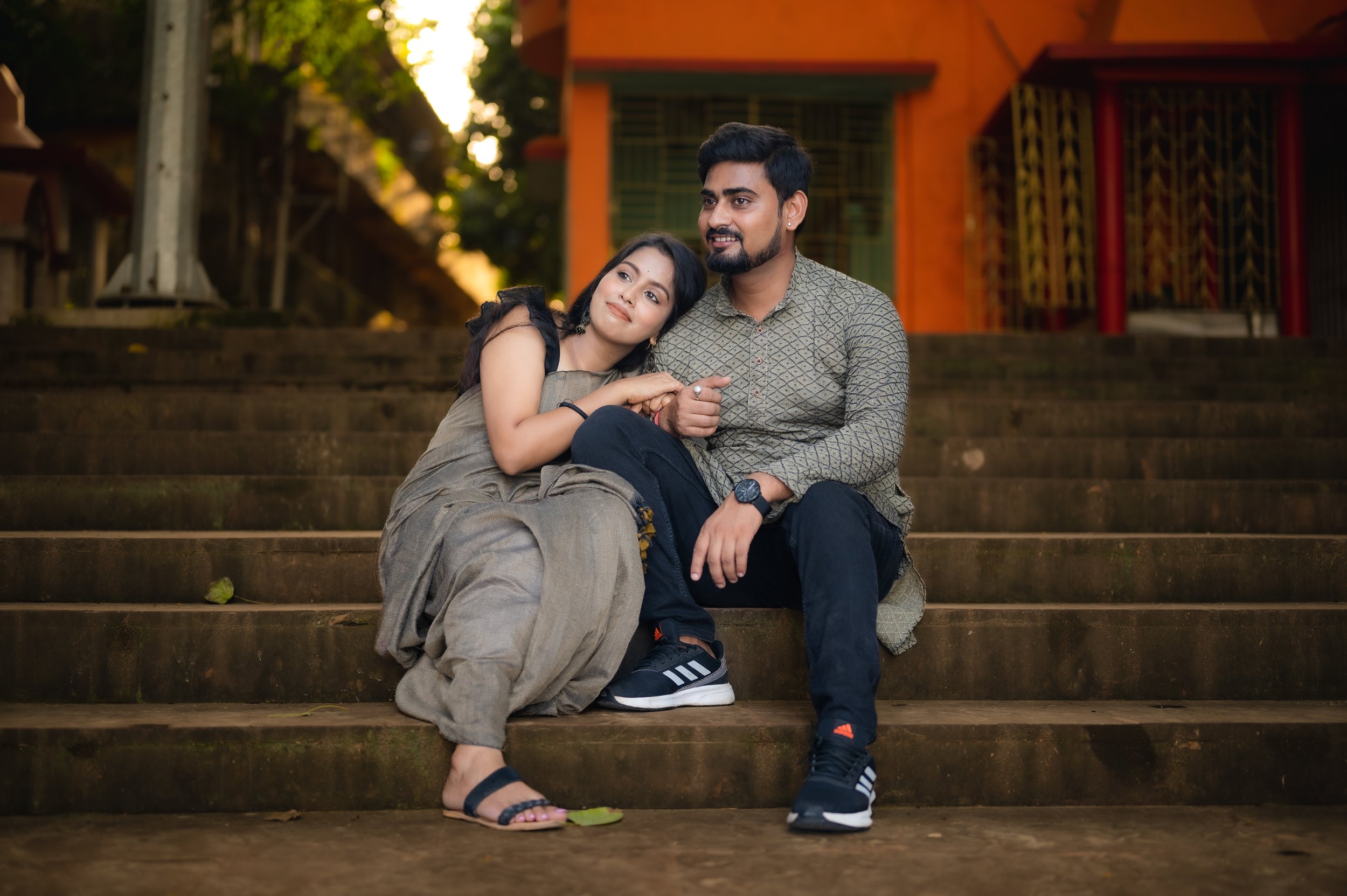 A young couple sitting on outdoor steps, smiling and enjoying each other's company during sunset.