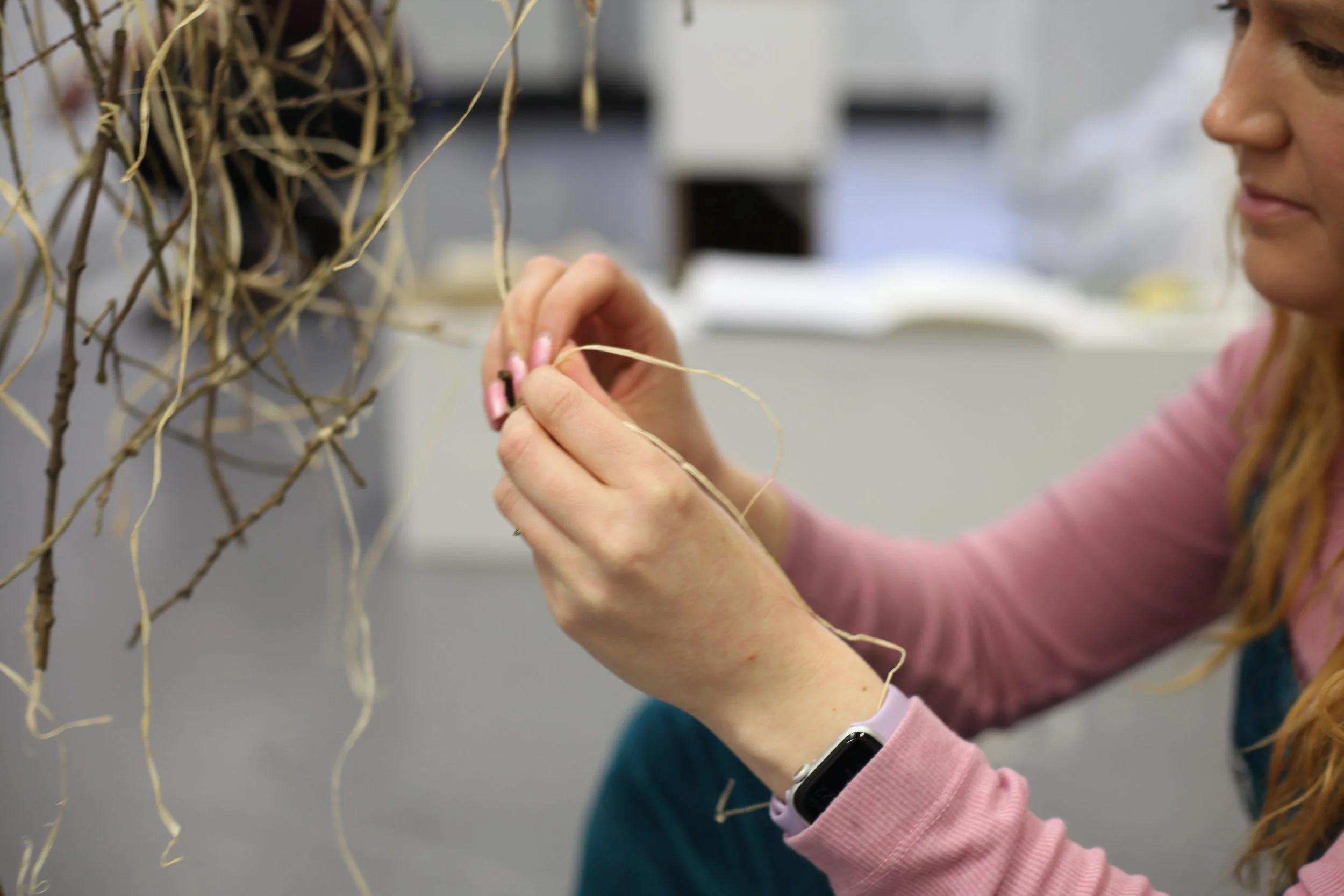 Image of hands knotting together raffia and fallen tree branches