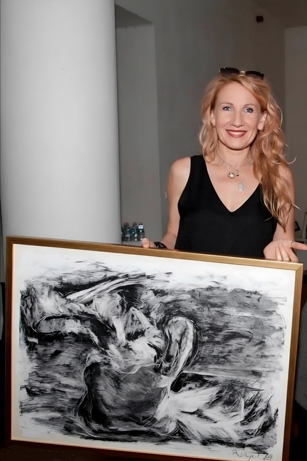 Anita Dangel holding a framed charcoal painting. Abstract black and white composition with sweeping gestural strokes, signed and dated 2024.