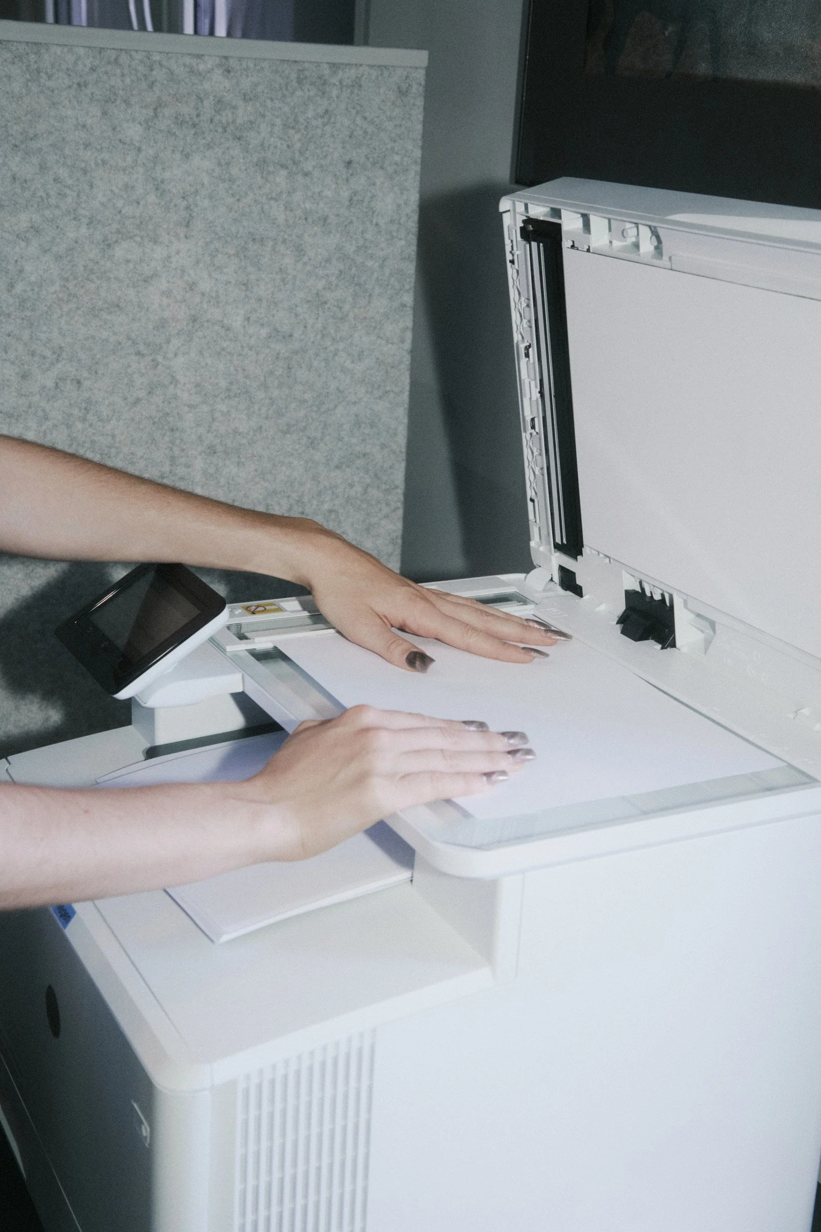 Person inserting paper into a white photocopier machine in an office environment.