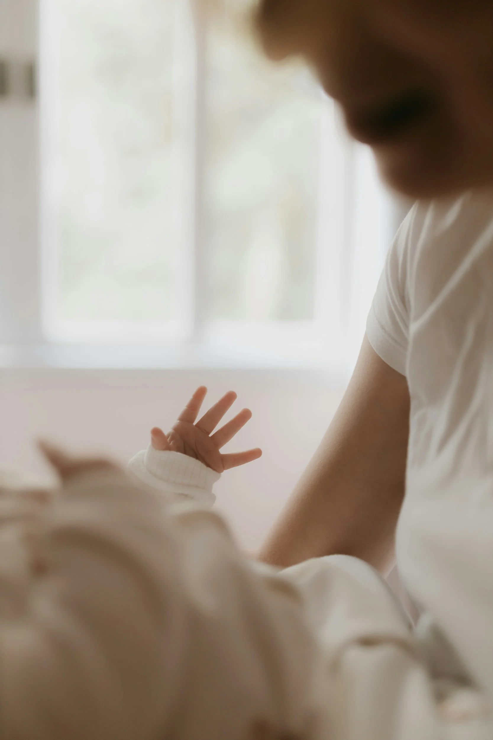 A mother reaching for her baby's hand in soft natural light, representing PAS recovery and the postpartum bond after a traumatic birth.
