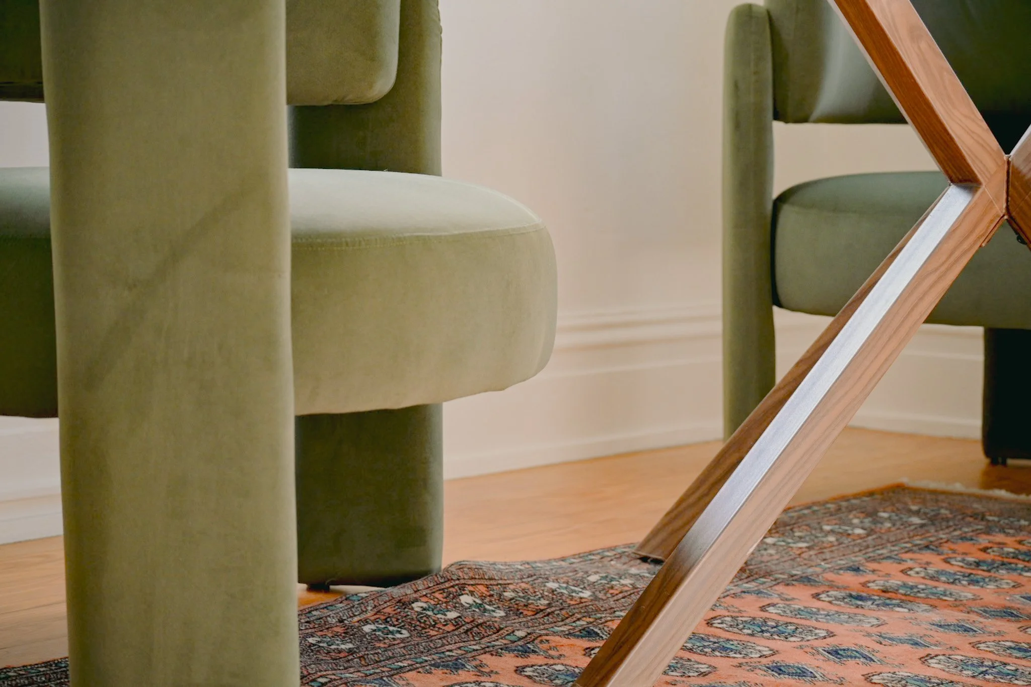 Close-up of green upholstered chairs around a wooden dining table, with a patterned rug on the hardwood floor.