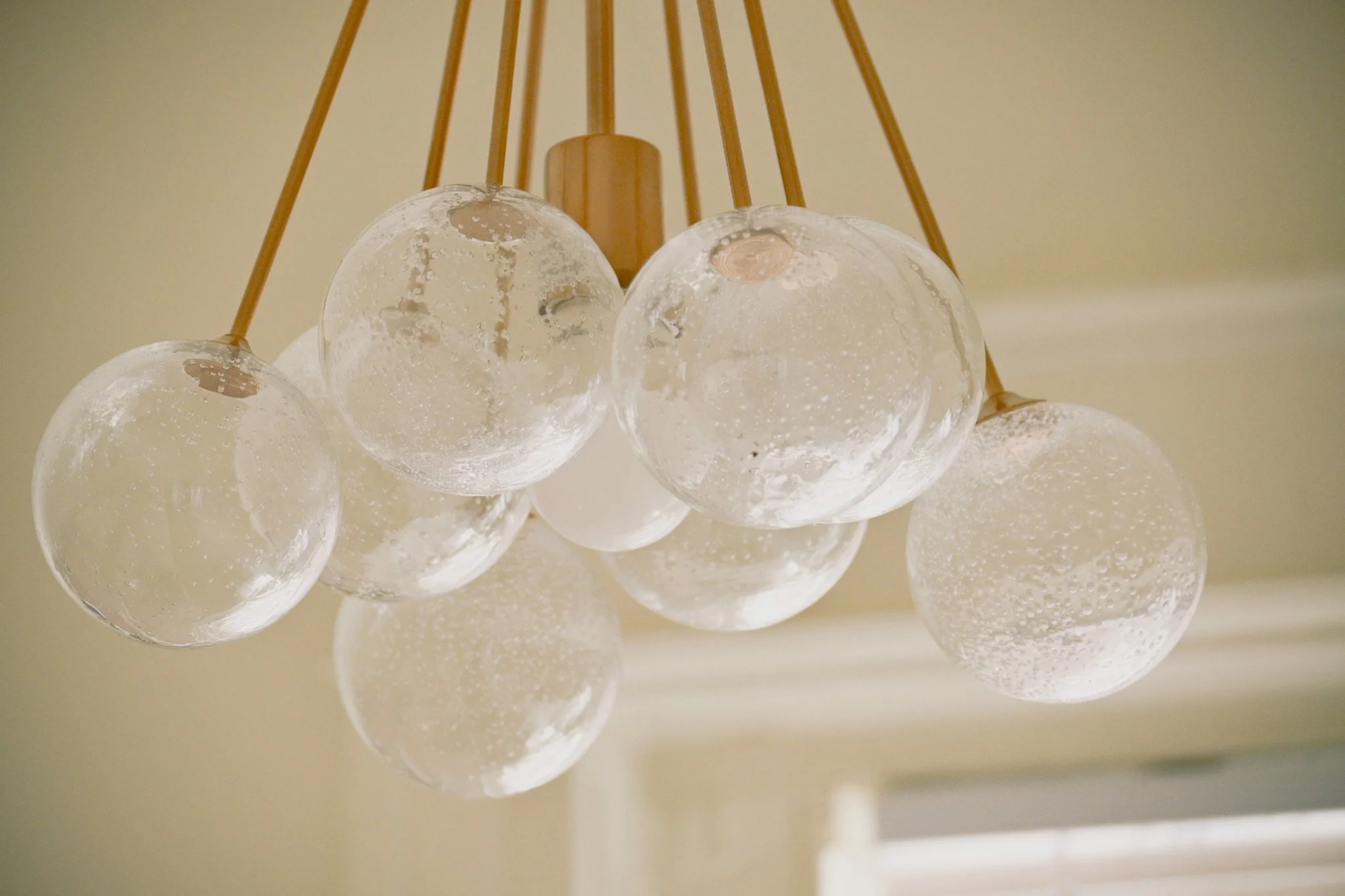 Close-up of a modern chandelier with multiple glass globes hanging from wooden rods, mounted on a ceiling.