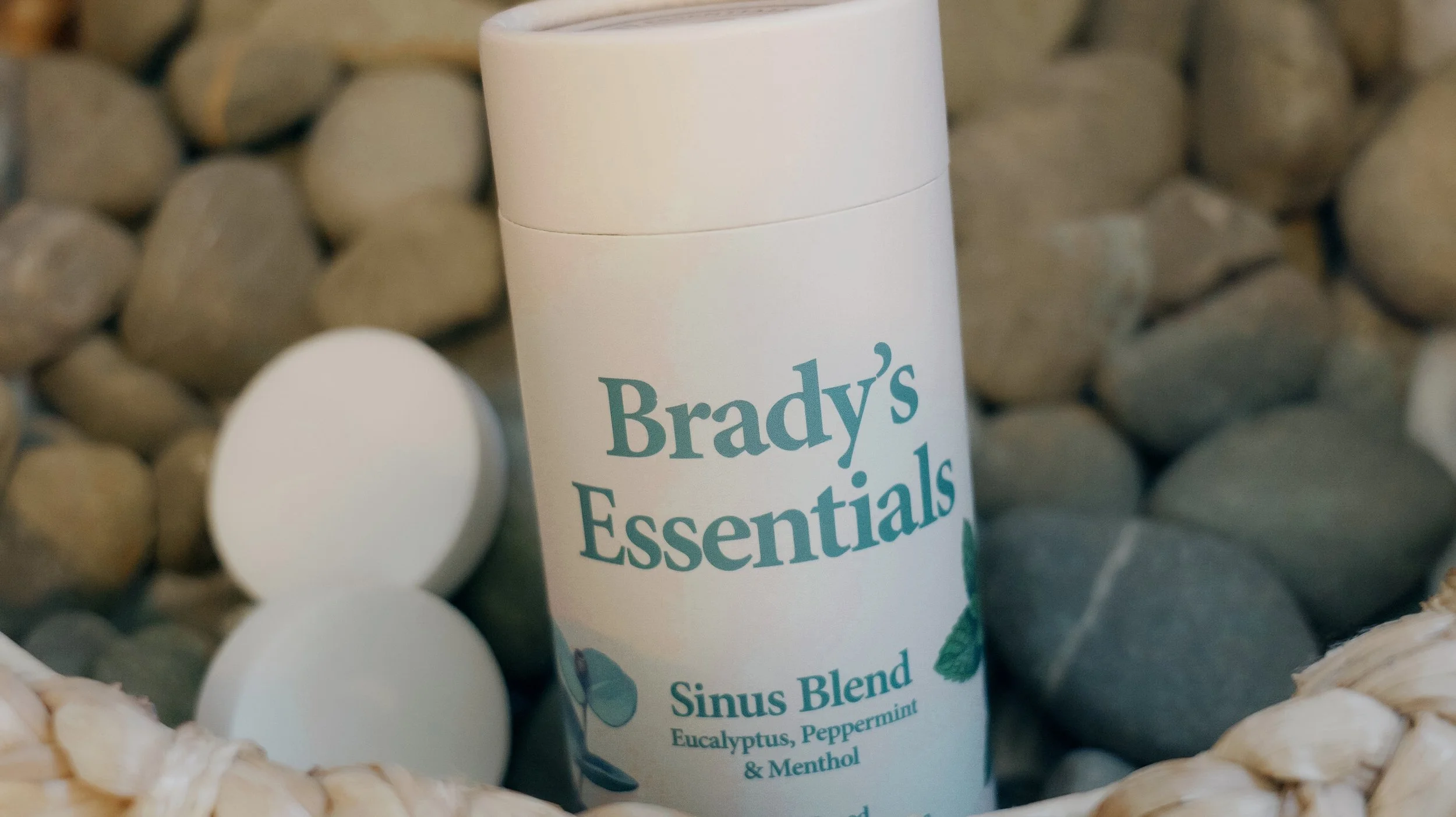A white bottle labeled 'Brady's Essentials' with a green leaf design, containing a sinus blend with eucalyptus, peppermint, and menthol, surrounded by white spherical bath bombs in a woven basket.