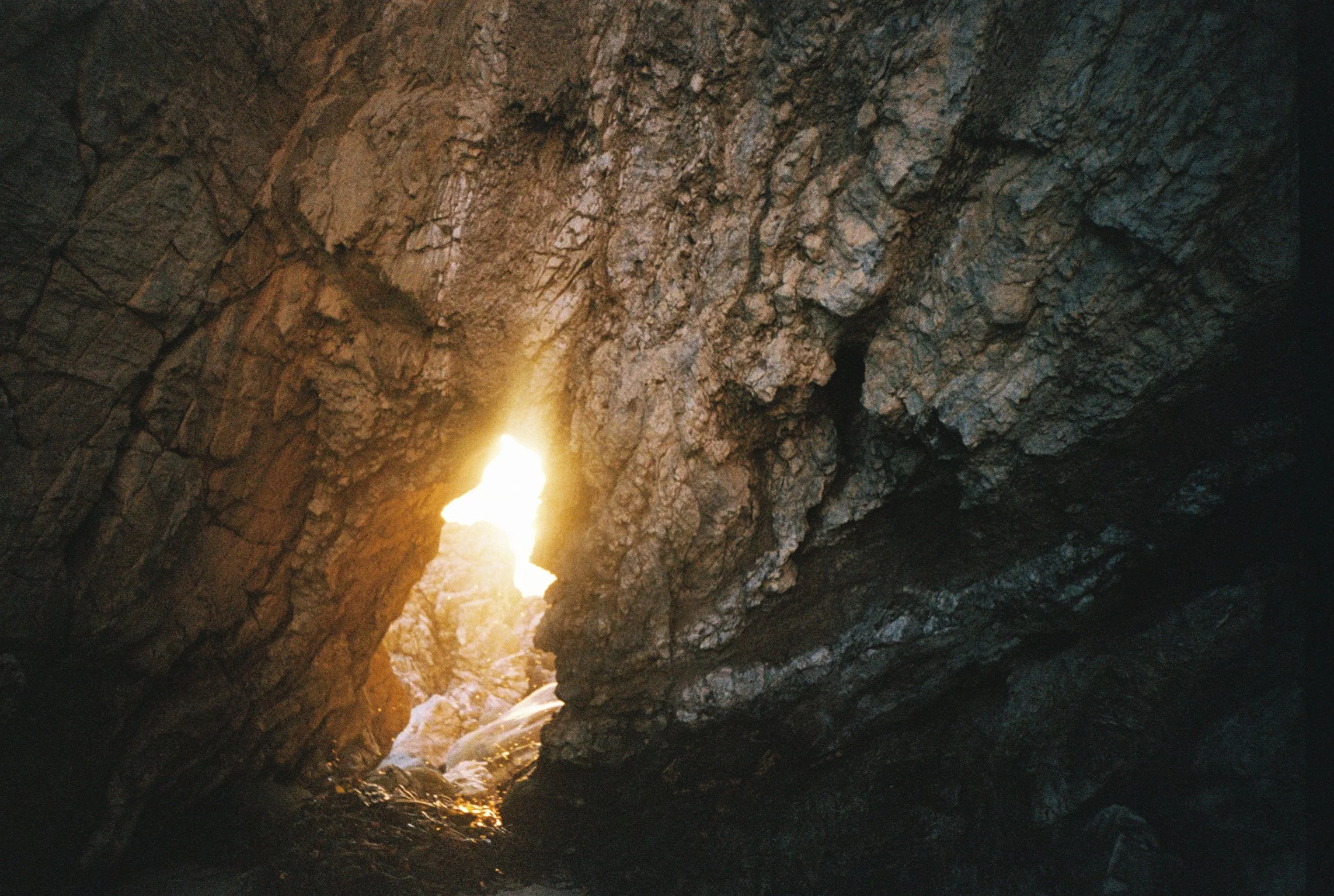Sunlight shining through a rocky cave opening with rugged, textured stone walls.