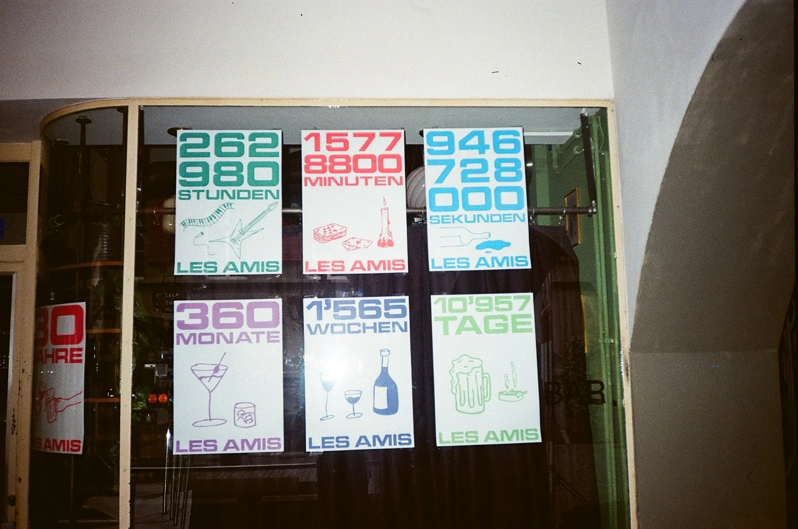 Norwegian language poster with various time, duration, and date related messages, featuring colorful text and simple illustrative icons, displayed on a window.