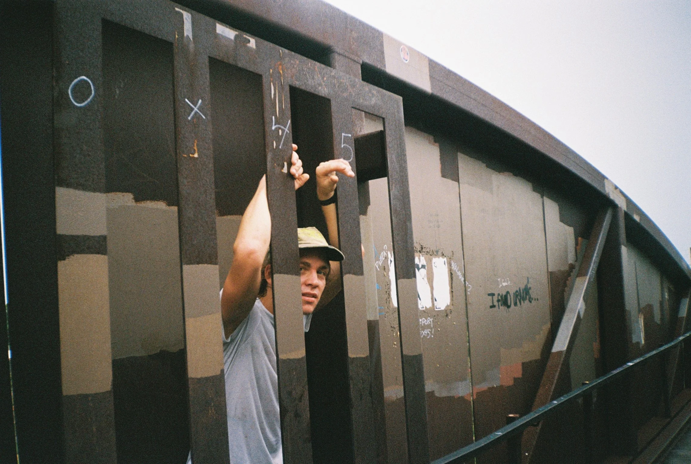 Person wearing a white shirt and a cap looking through black iron bars.