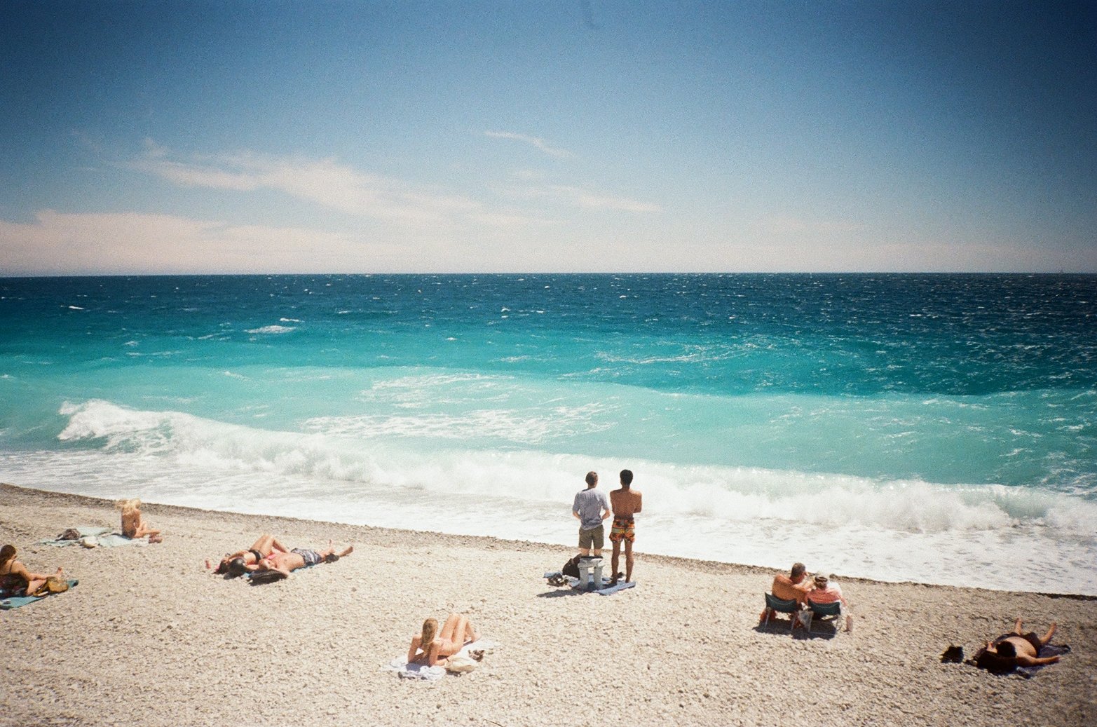 People relaxing on a beach with clear blue ocean and sky in the background.