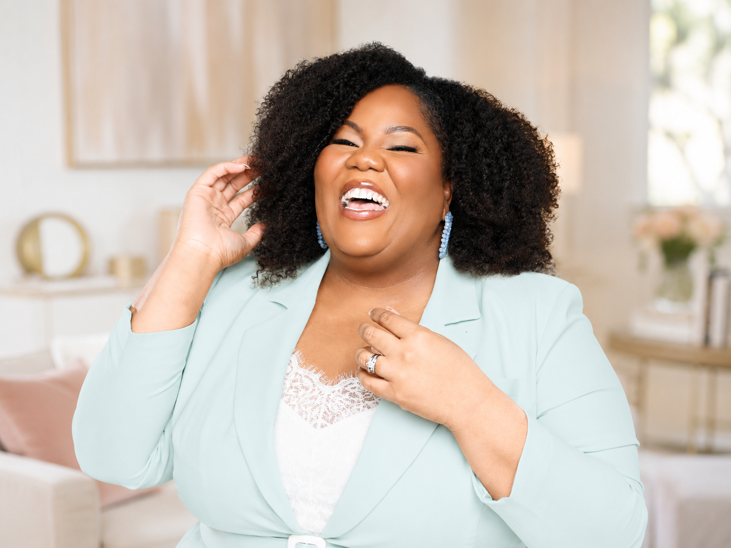 Amanda Ross-Hardin with curly hair and blue earrings laughing indoors.