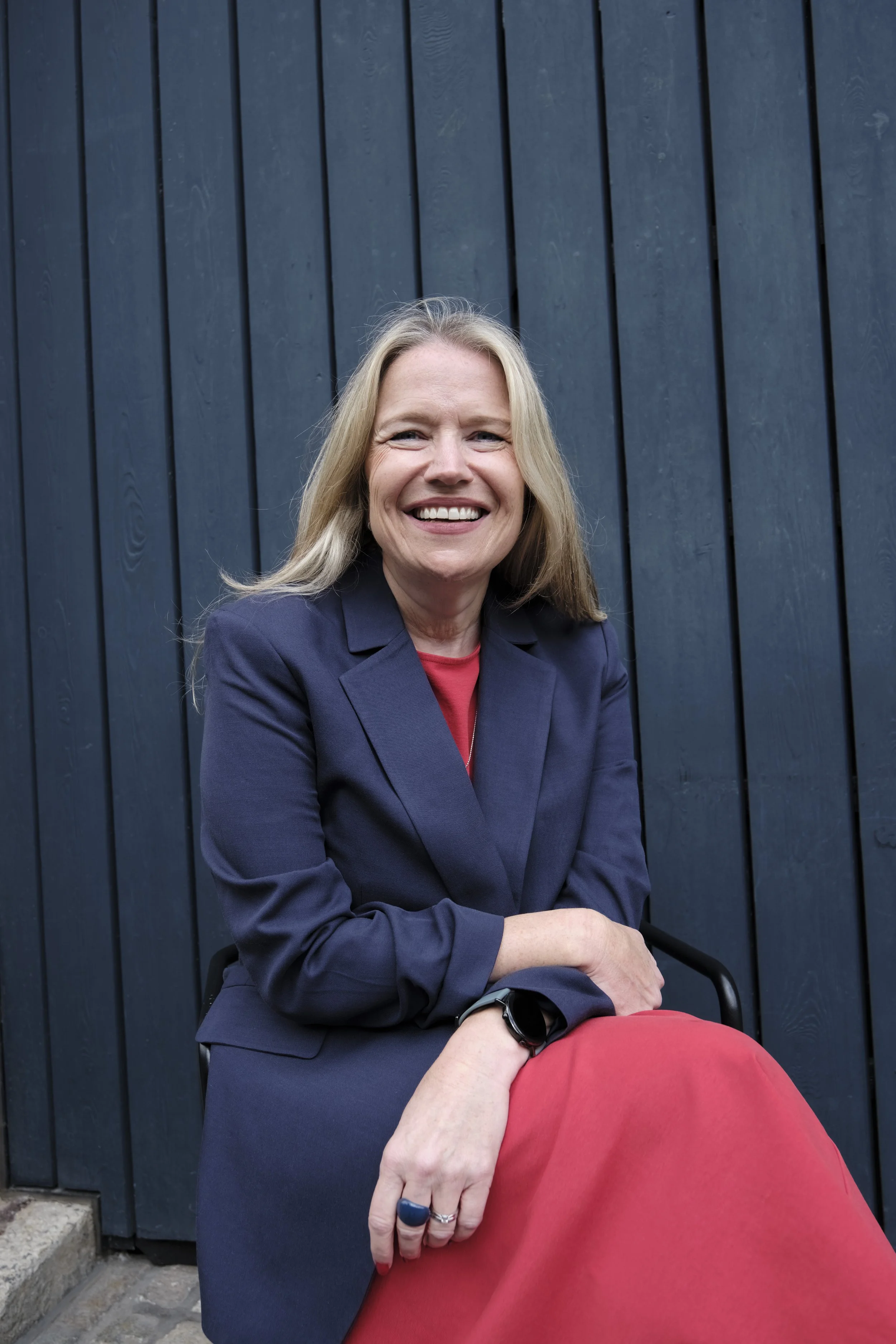 Debbie Porter sitting outdoors against a dark blue wooden wall.