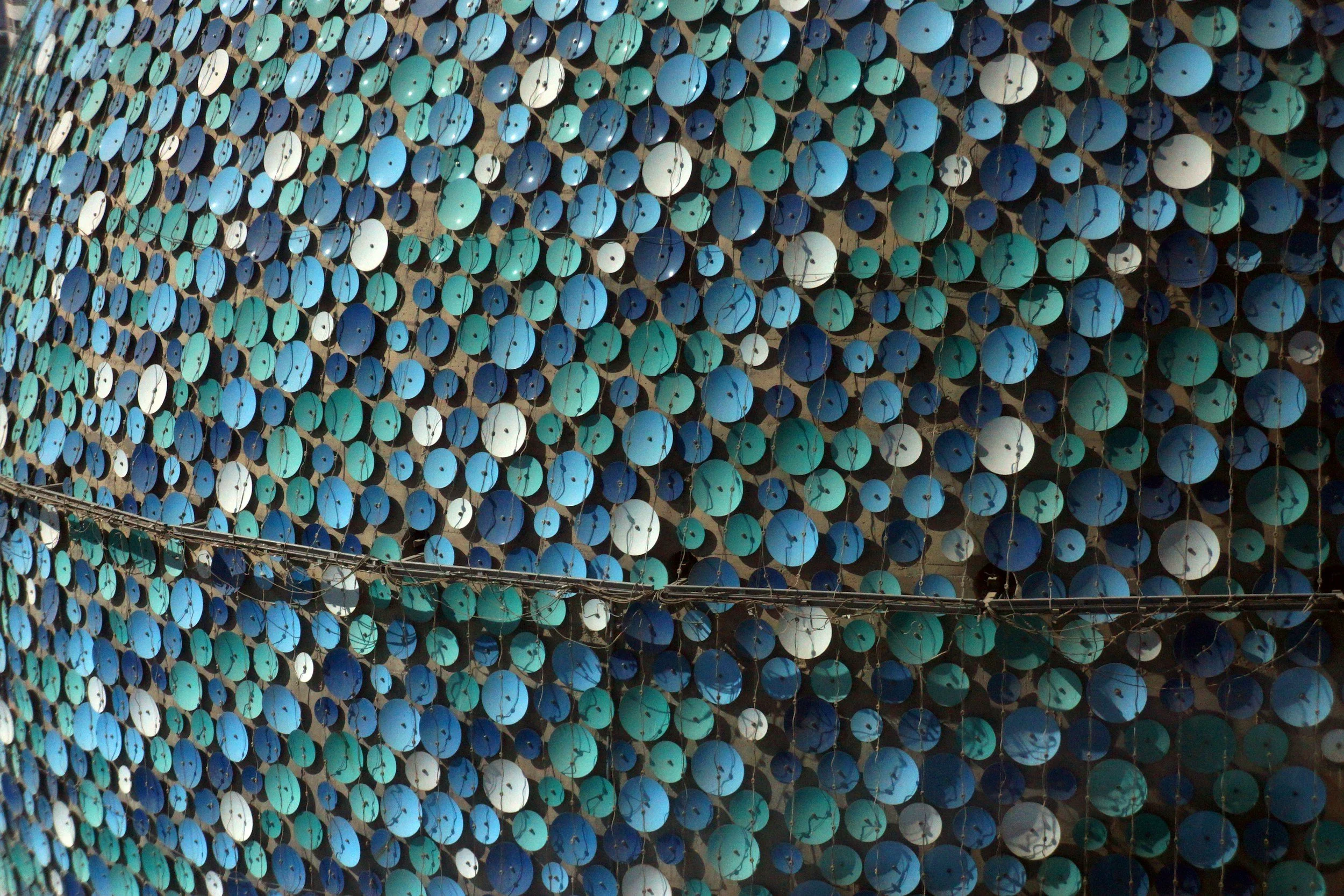 A large outdoor installation in Kuwait made of numerous blue, teal, white, and black circular objects, possibly umbrellas or discs, arranged on a wall or structure.