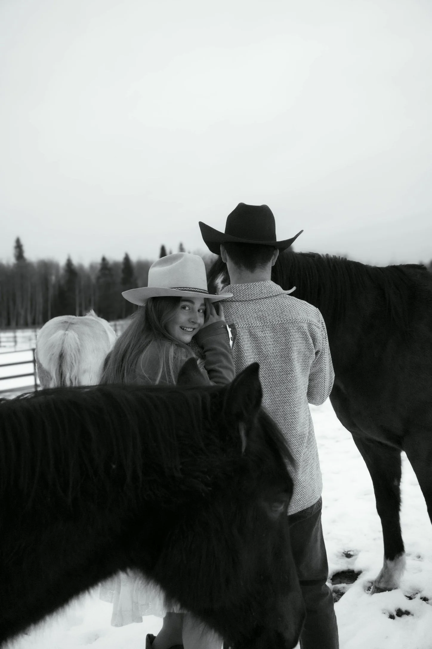 People in cowboy hats standing outdoors in a snowy landscape with trees in the background, accompanied by a black and white cow.