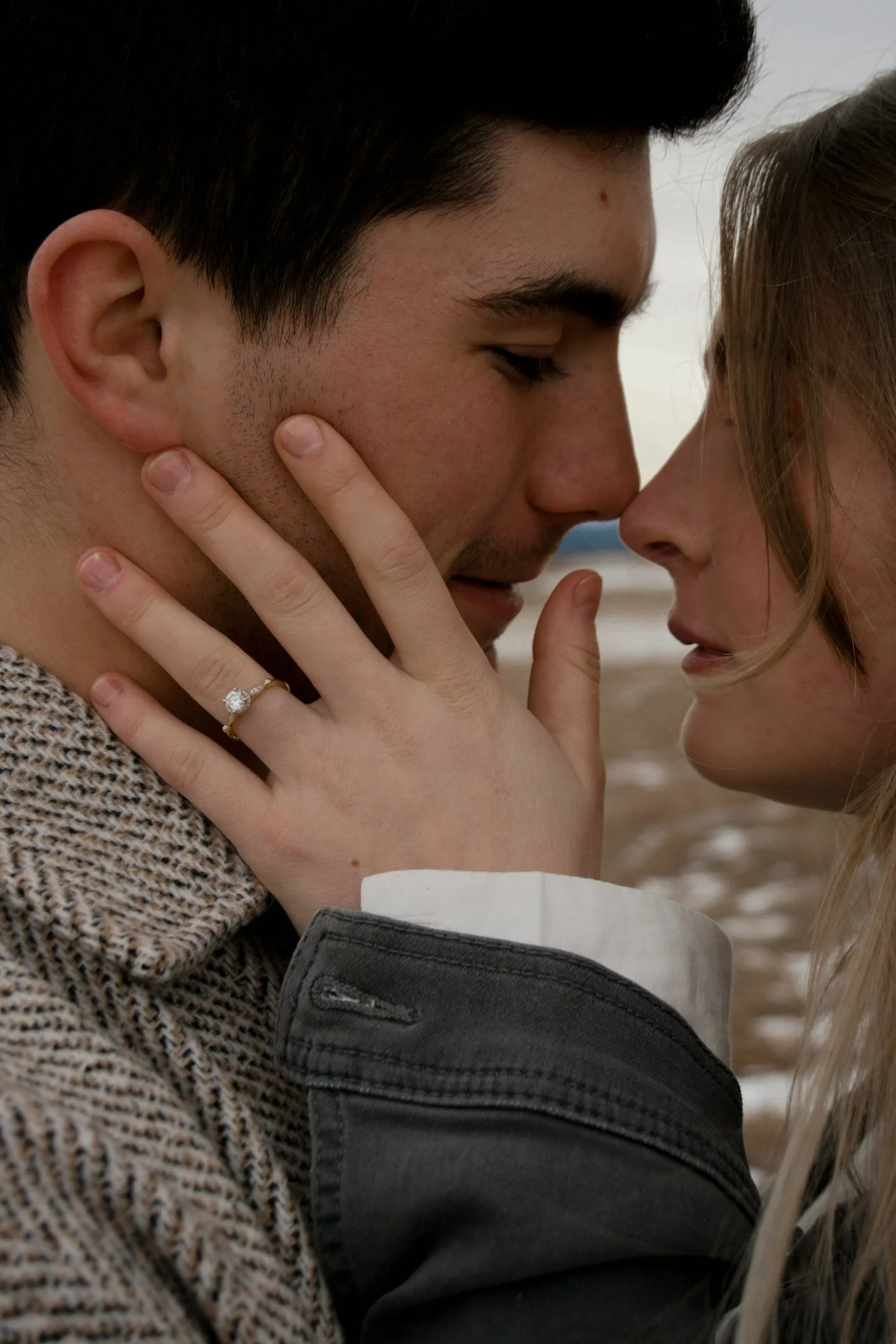 A close-up of a couple touching foreheads and gazing into each other's eyes, with one woman's hand gently on the man's cheek, including a diamond ring on her finger.