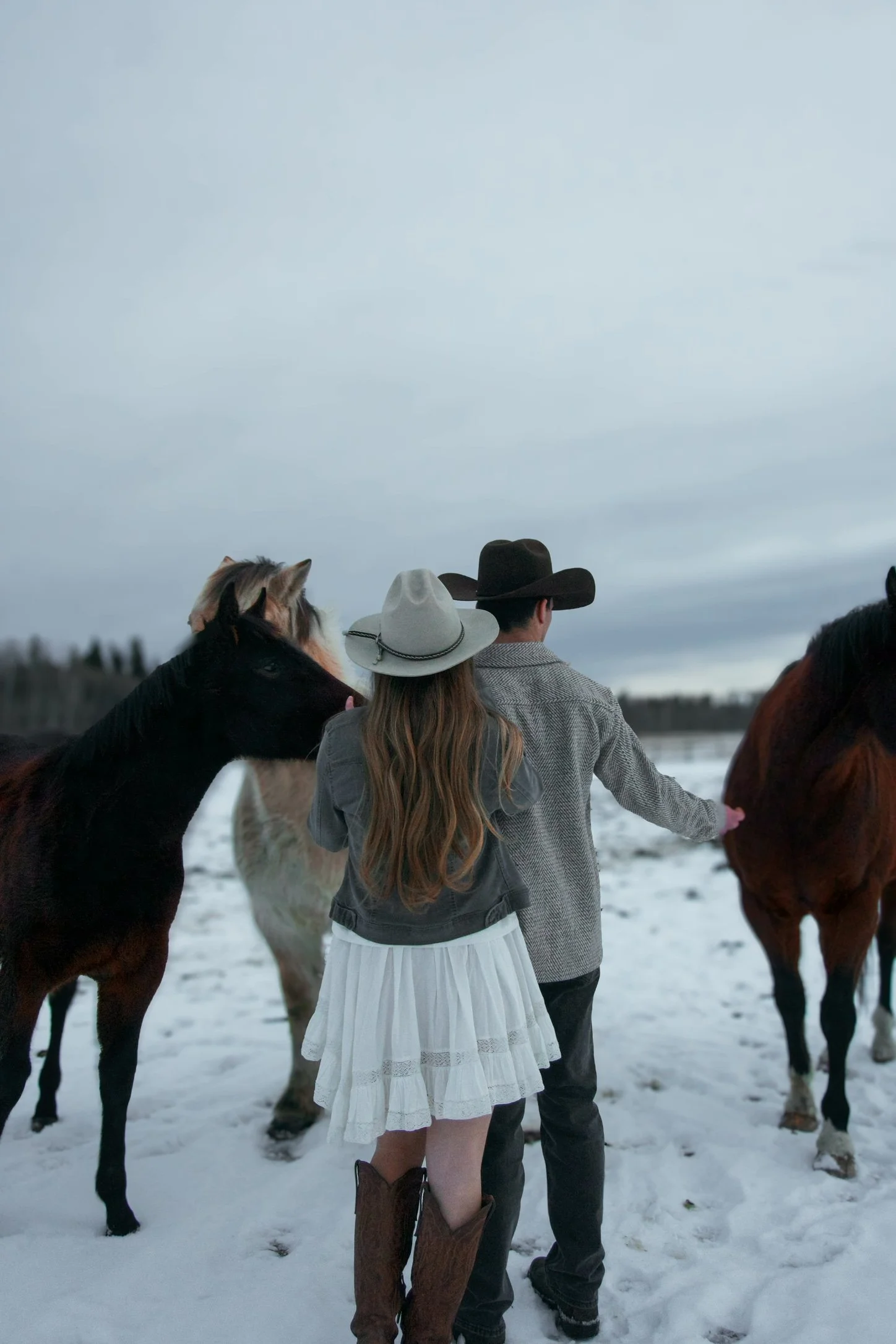 Two women and a man with horses in a snowy outdoors setting, wearing cowboy hats and warm clothing.