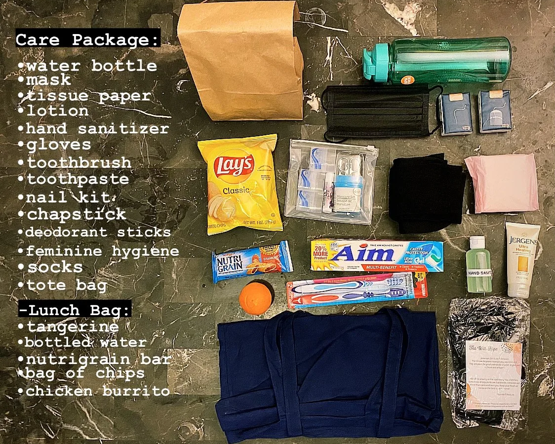 An organized collection of personal items and a care package laid out on a dark marble surface, including water bottle, mask, tissue paper, lotion, hand sanitizer, gloves, toothbrush, toothpaste, nail kit, chapstick, deodorant sticks, feminine hygiene products, socks, tote bag, and items for lunch such as a tangerine, bottled water, NutriGrain bar, chips, and chicken burrito.