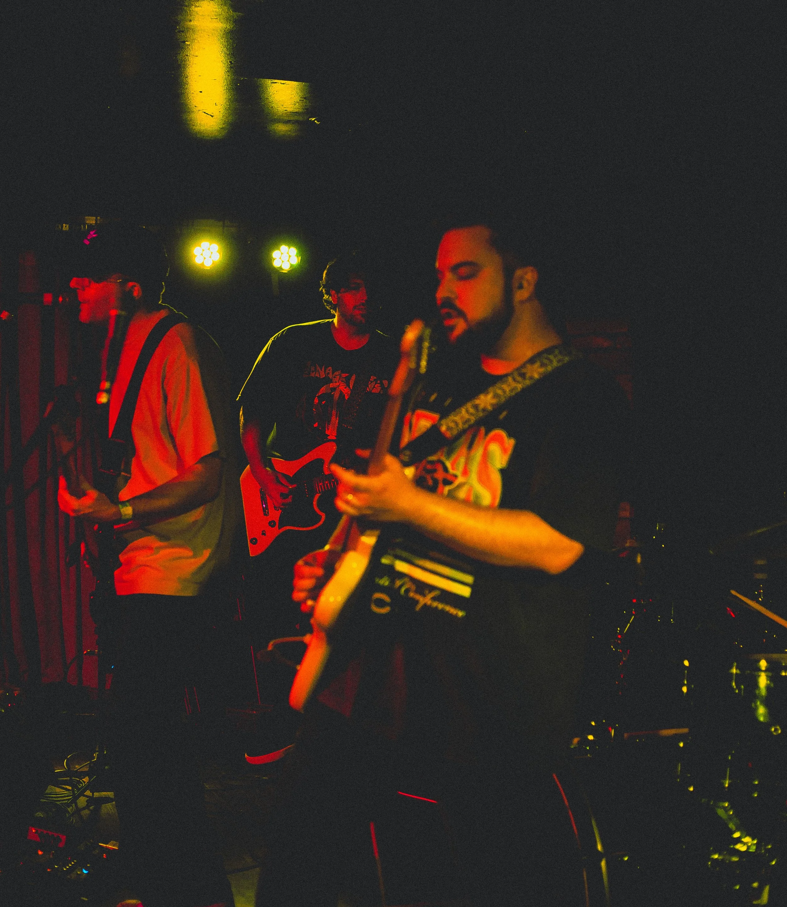 People playing guitars on stage with bright yellow and green stage lights illuminating the scene at night.
