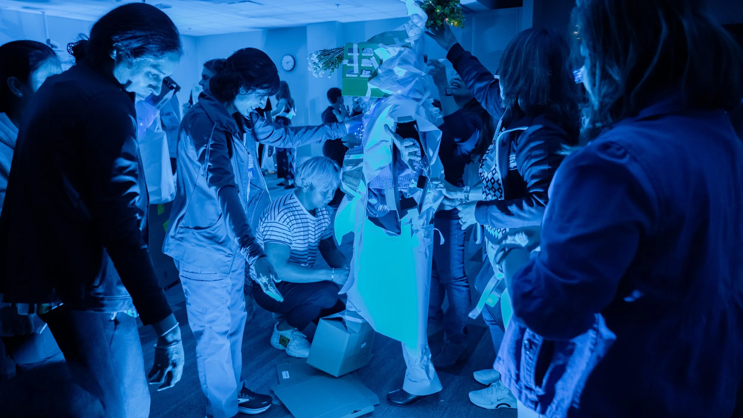 People gathered around a display at an event, with blue lighting and a person holding flowers.