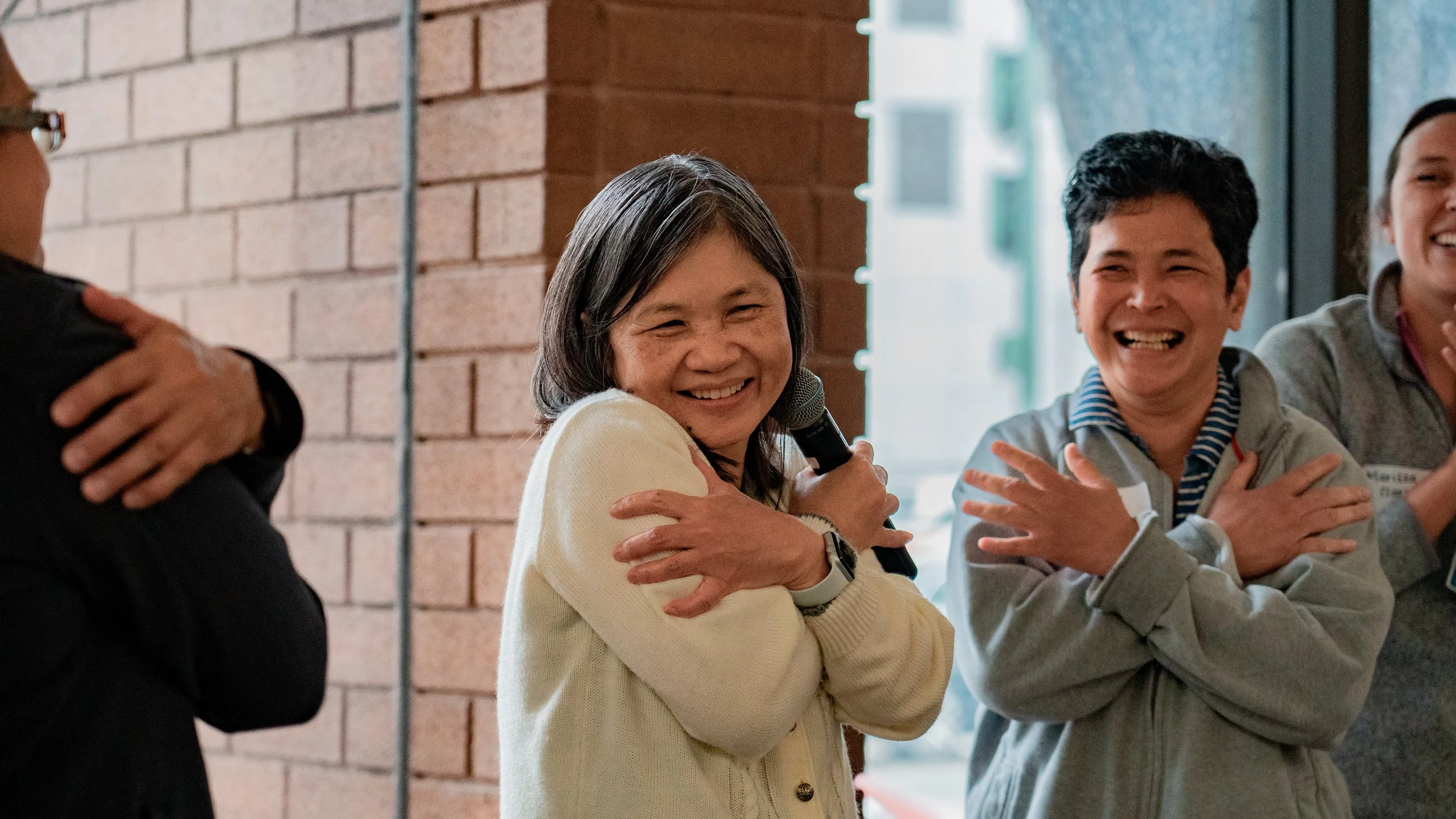 Group of people smiling and hugging each other during a social gathering or event inside a building with a brick wall.