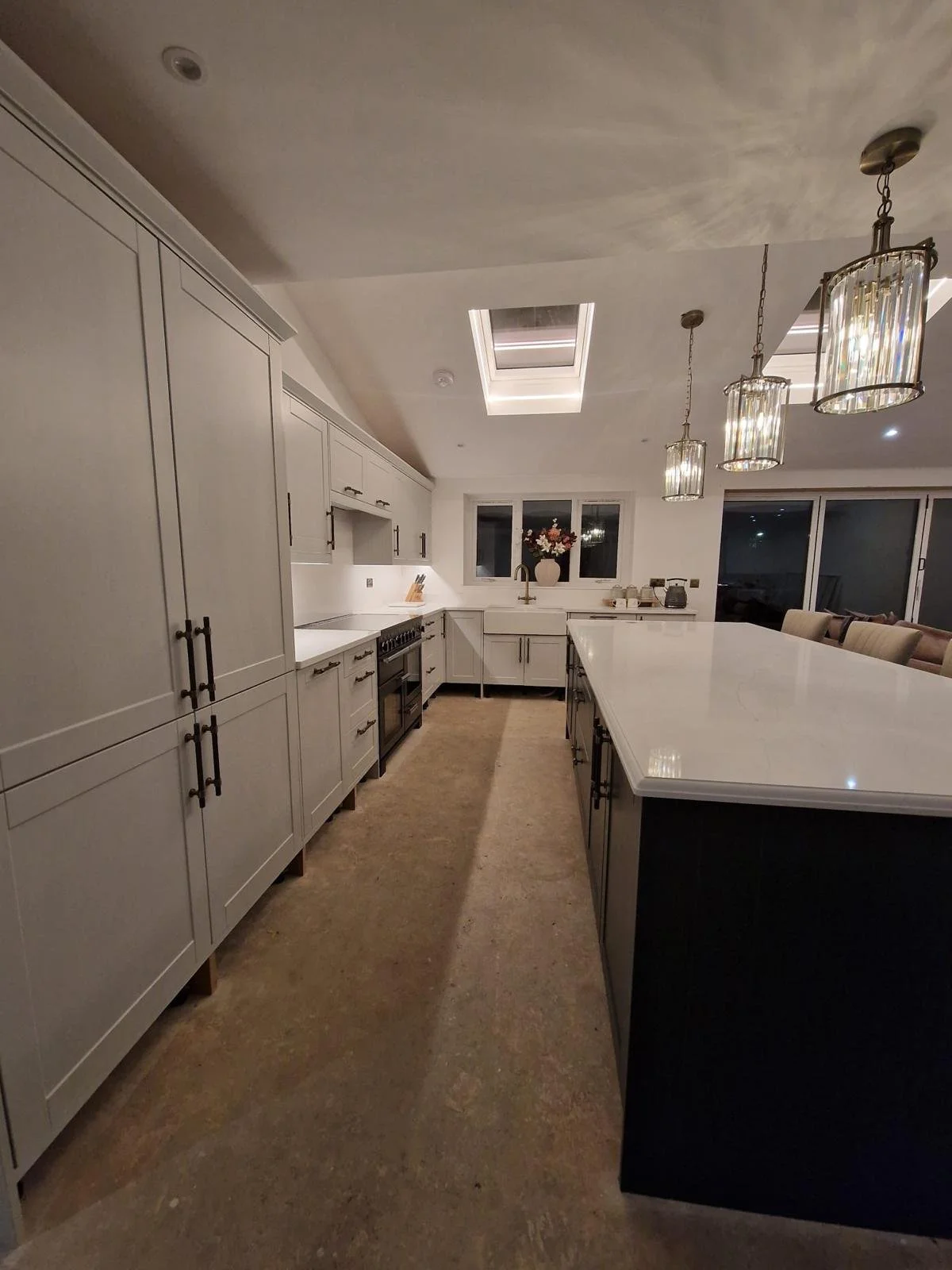 Modern kitchen with white cabinets, a large white island, pendant lights, and a window with a vase of flowers.