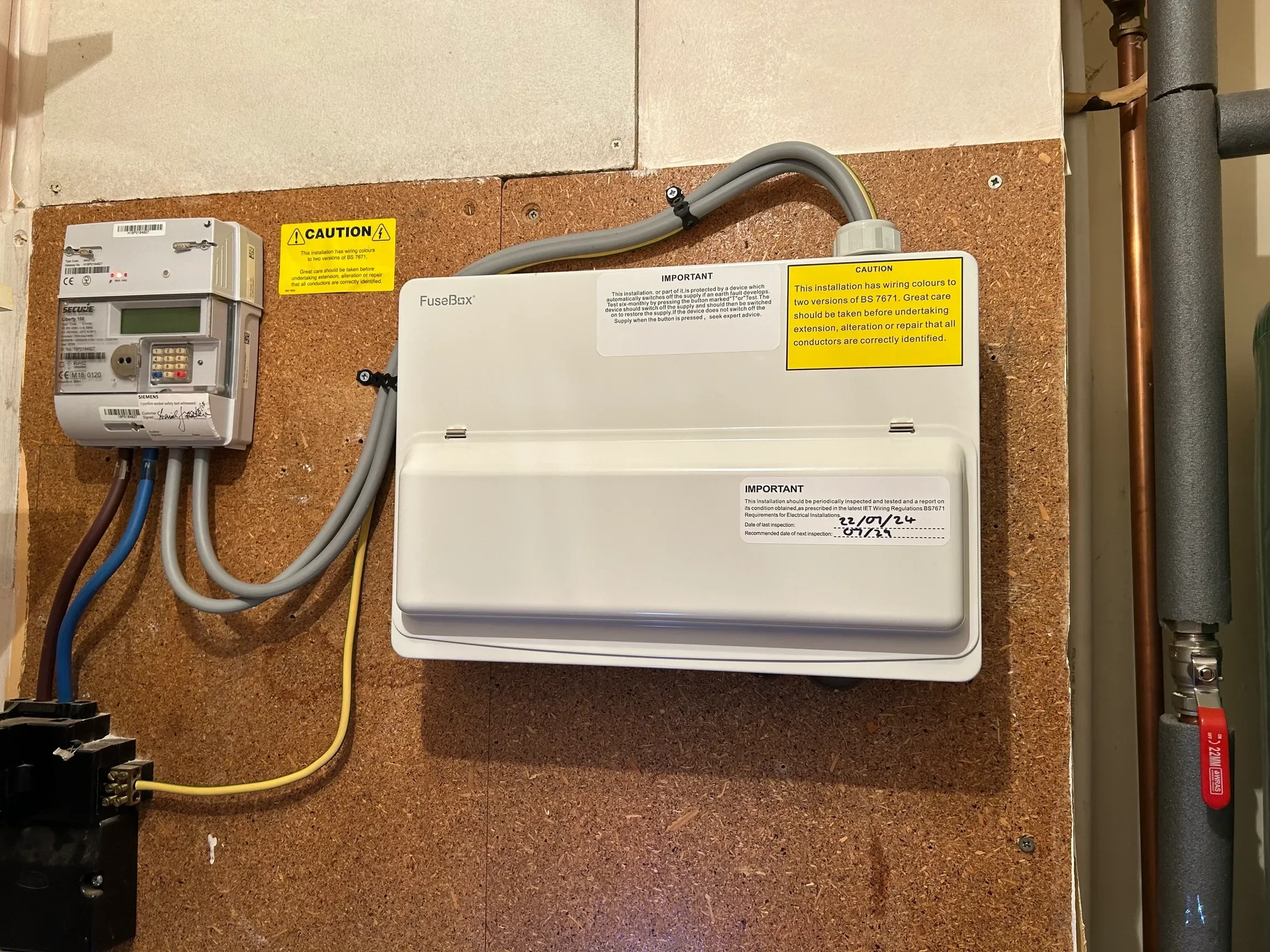 Electrical control panel with a digital meter, wiring, and yellow caution labels on a brown cork backing.