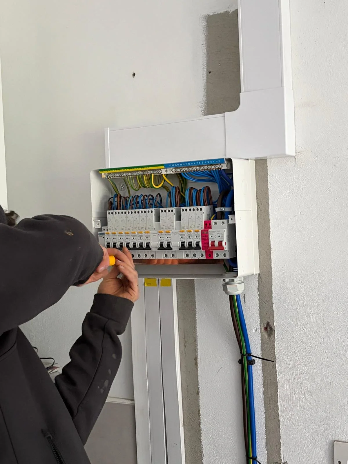 Technician working on an electrical panel with circuit breakers and wiring inside a white enclosure.