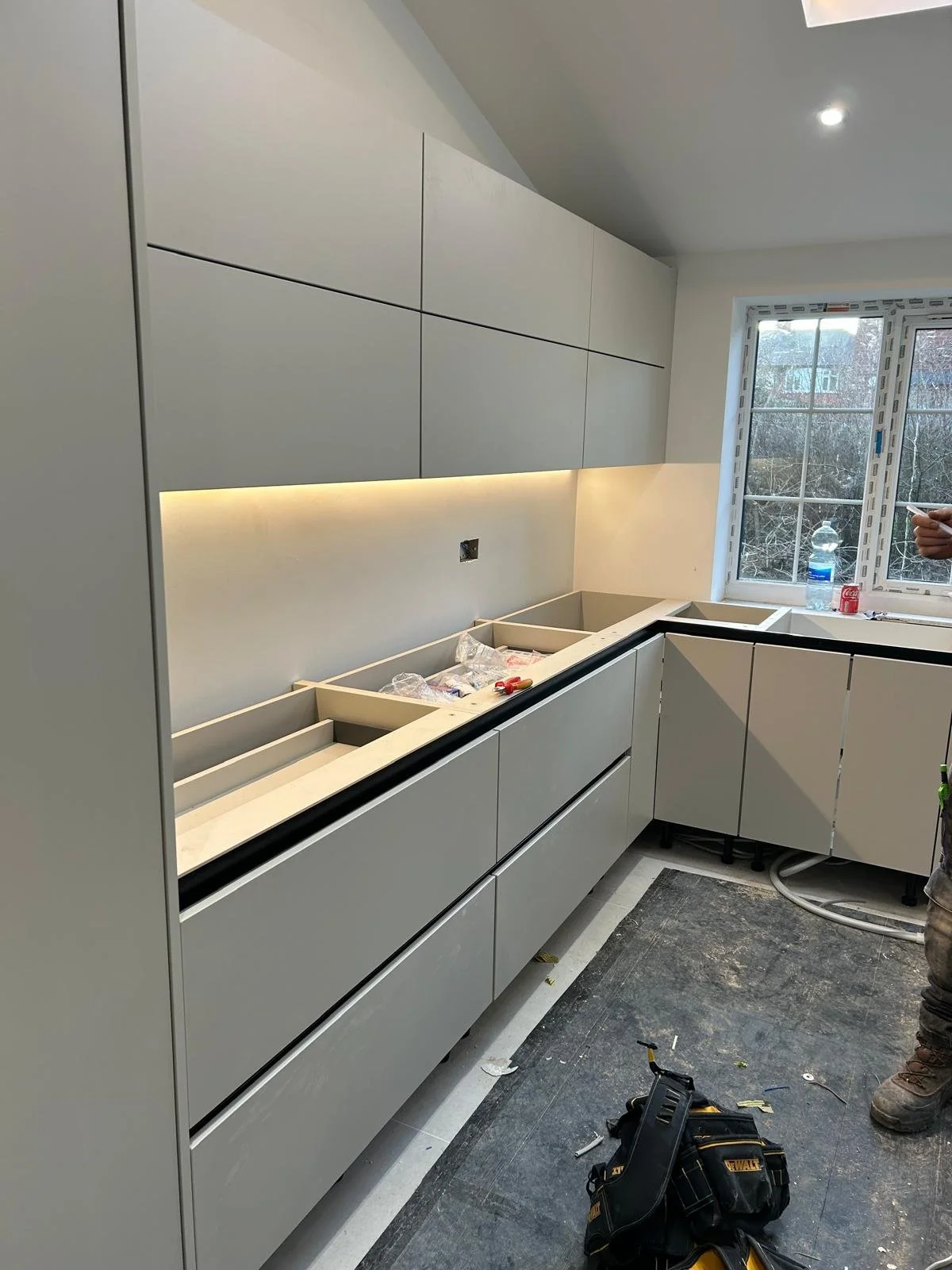 Kitchen under construction with new gray cabinets, a window, and construction tools on the floor.