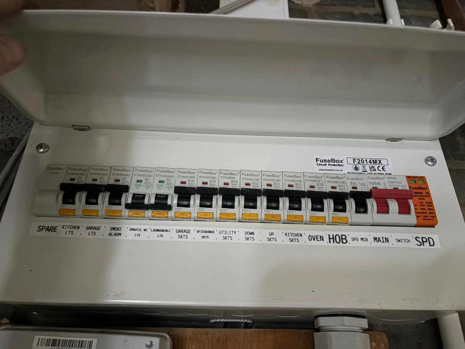 An electrical fuse box with multiple fuses and switches, labeled with various areas like kitchen, garage, utility, and oven, housed inside a white metal enclosure with a hinged door.