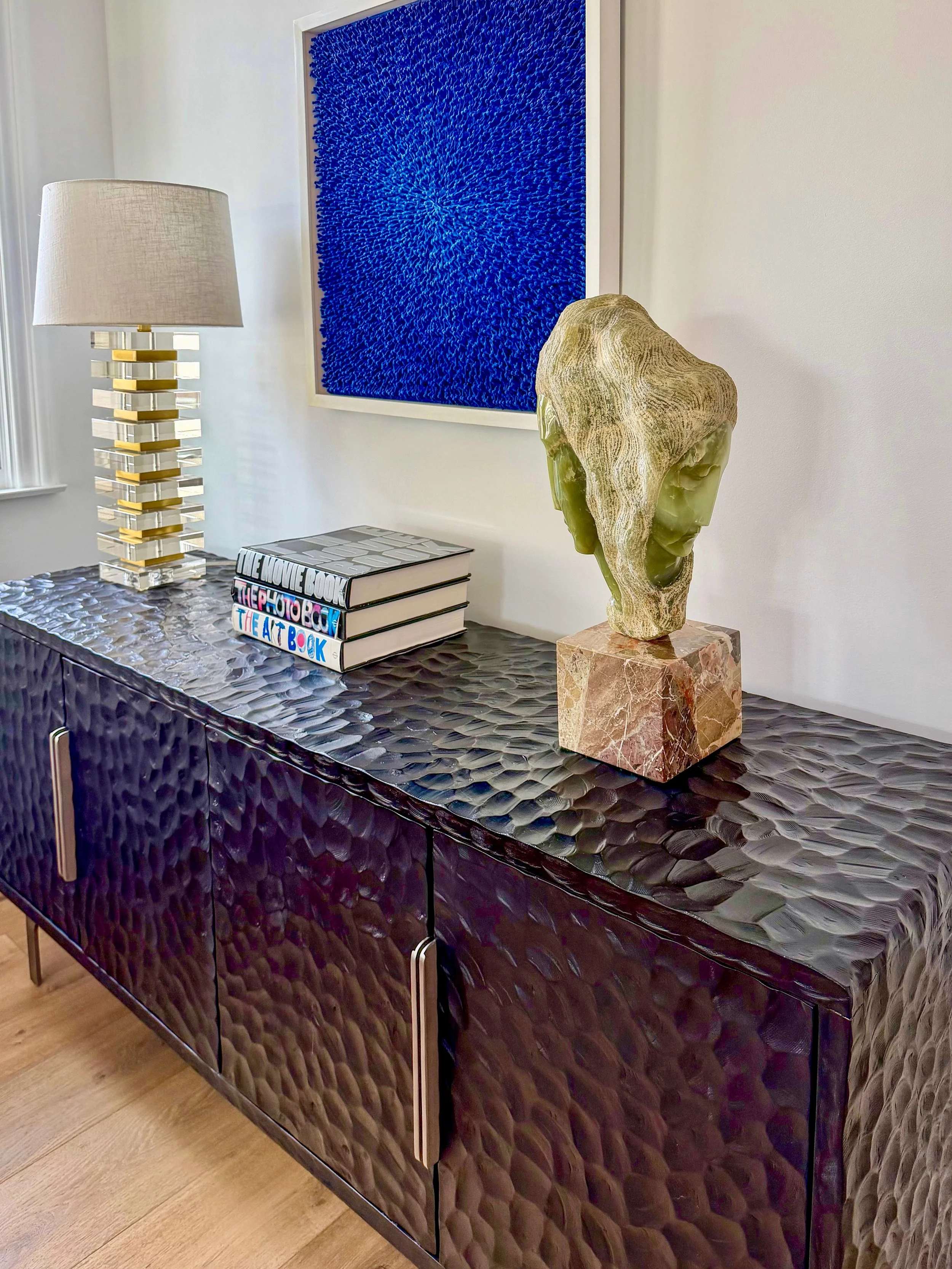 Black textured sideboard with gold and glass lamp on a white wall background