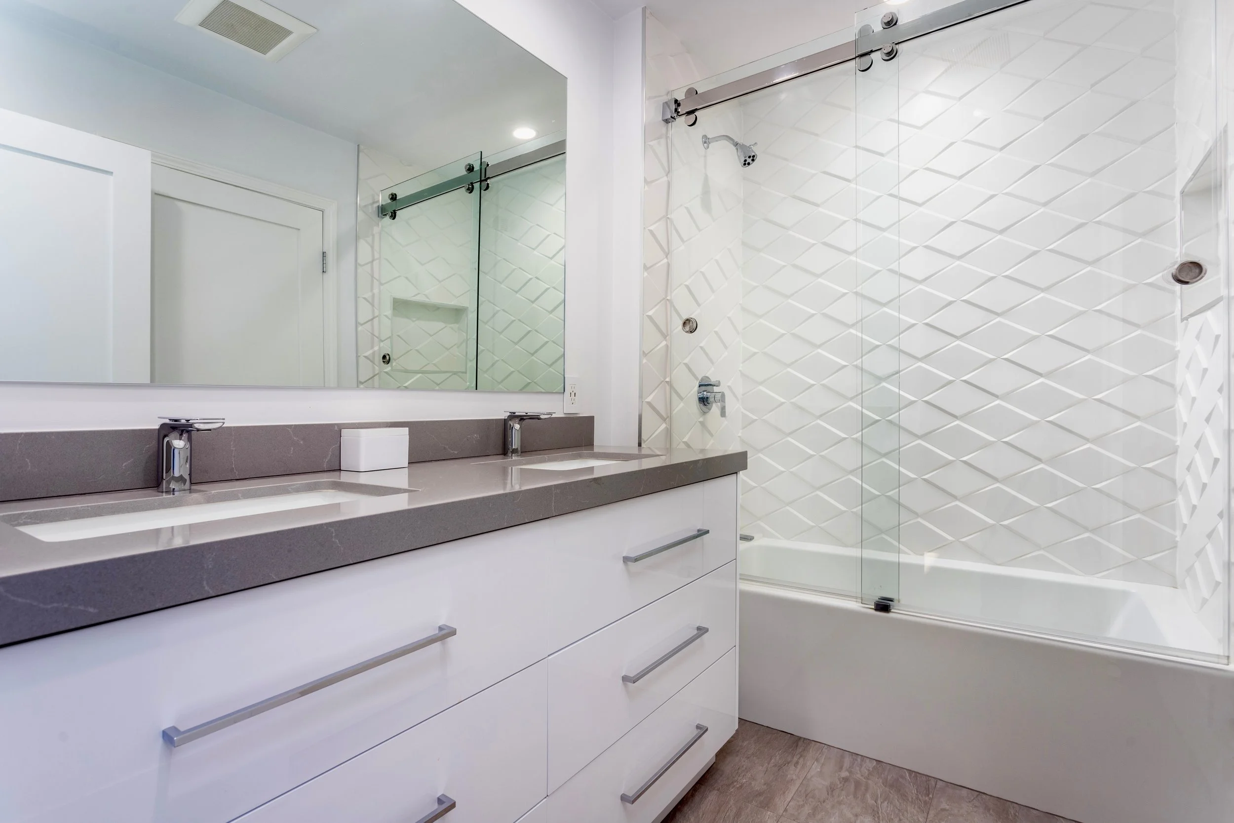 Bathroom with white vanity, gray countertop, large mirror, two sinks, and a glass-enclosed shower with tiled walls.