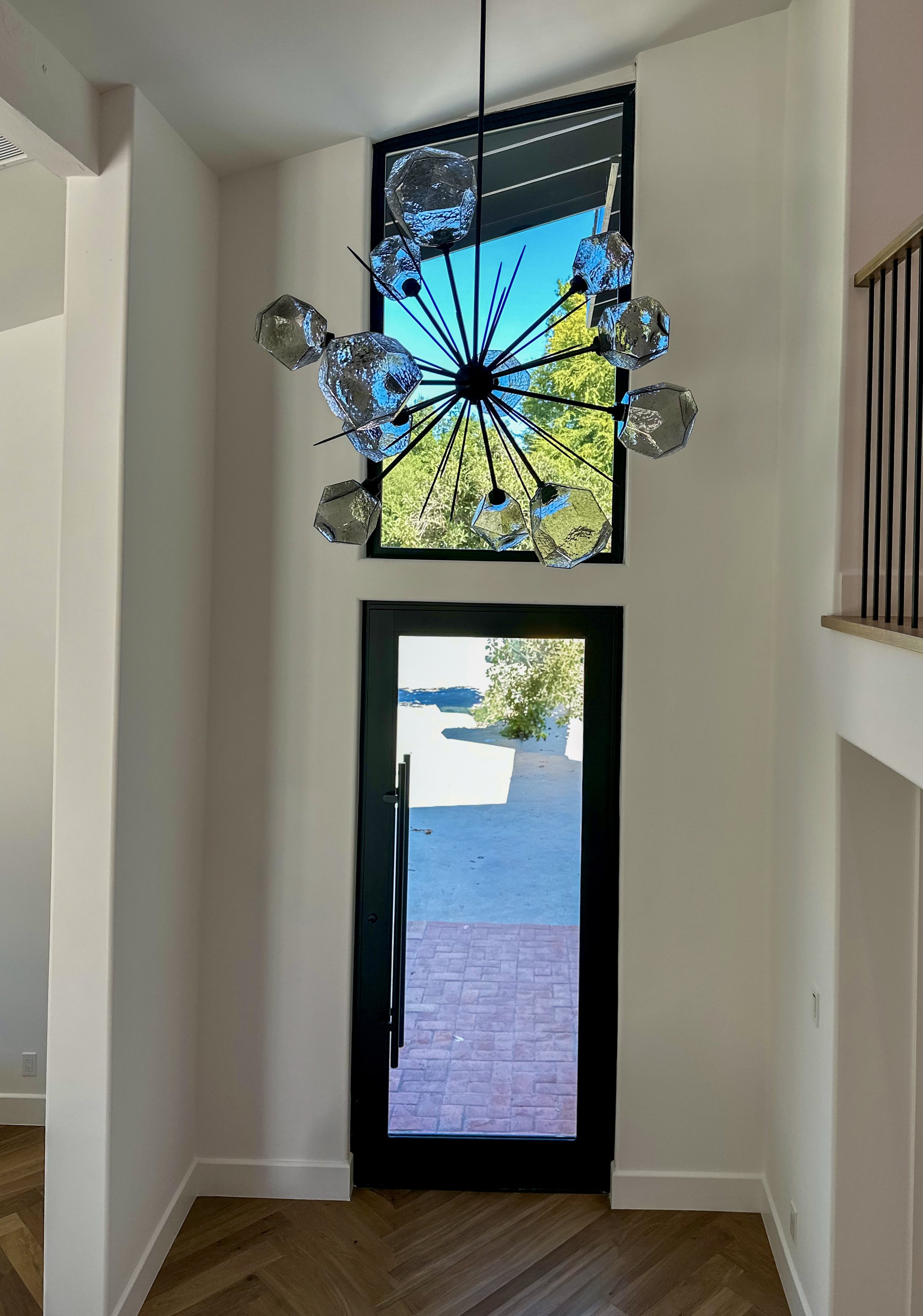 Interior view of an entryway with a large glass door leading outside, bright natural light, and wooden flooring.