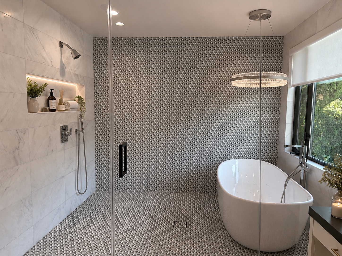 Modern bathroom with a freestanding soaking tub next to a large window, textured gray tiles on the wall and floor, a chandelier, and a built-in shelf with toiletries and greenery.