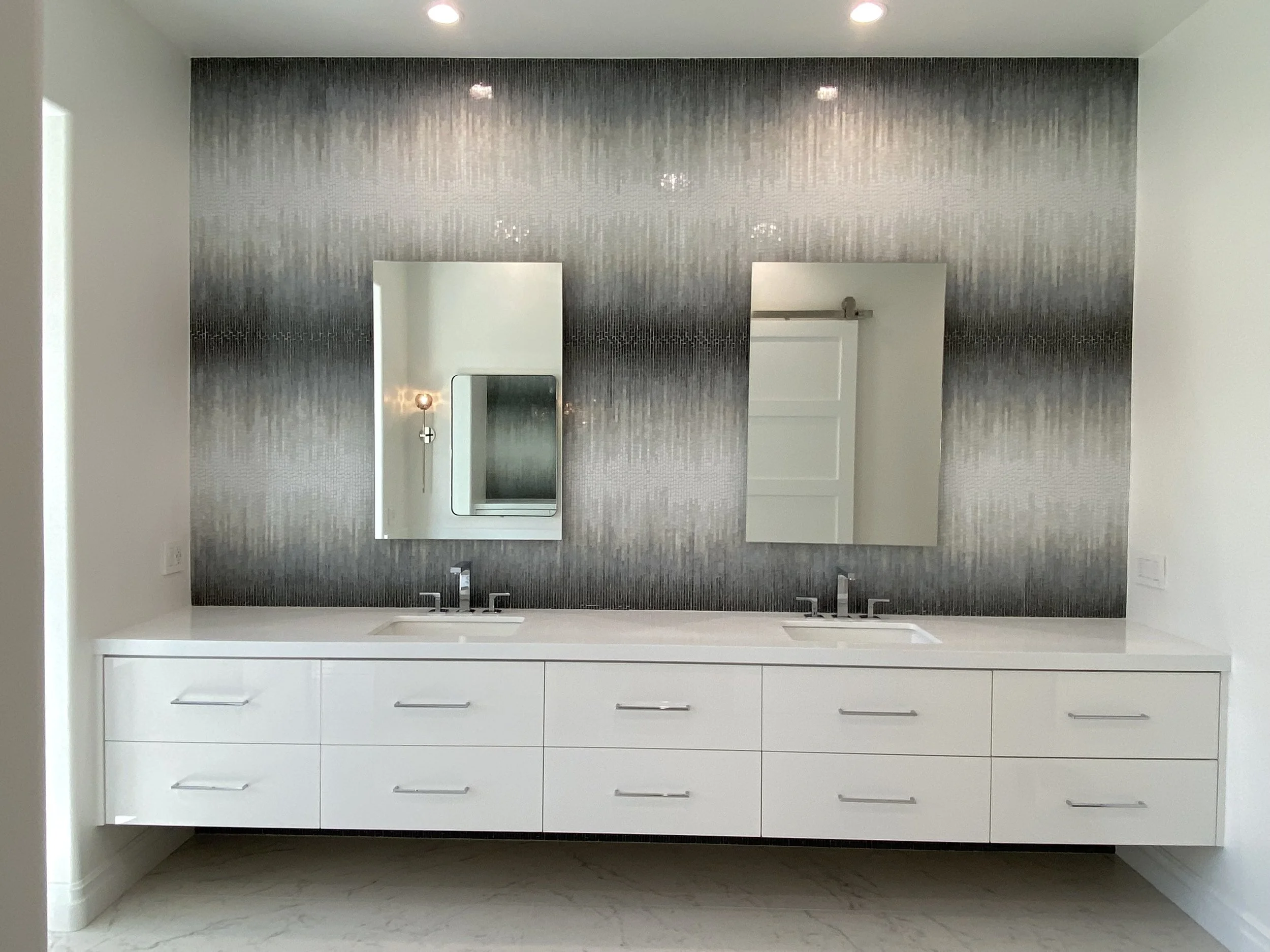 Modern bathroom vanity with white cabinets, a dark tiled backsplash, a rectangular mirror, and a small wall mirror above the sink.