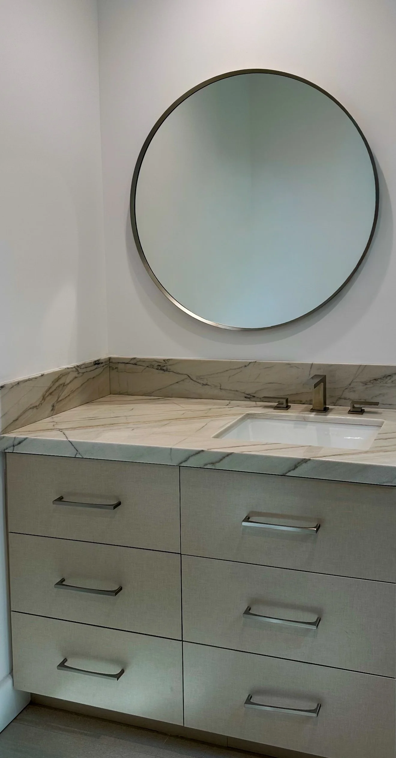 Modern bathroom vanity with marble countertop, oval mirror, and dual faucet sinks.