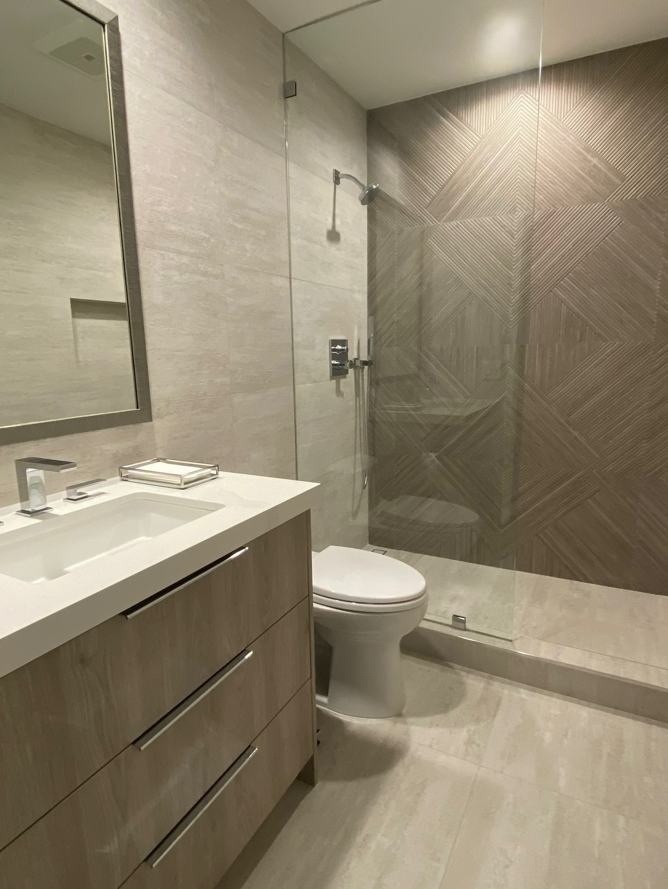 Modern bathroom with a white sink vanity, a toilet, a glass-enclosed shower with wood textured tiles, and beige wall tiles.