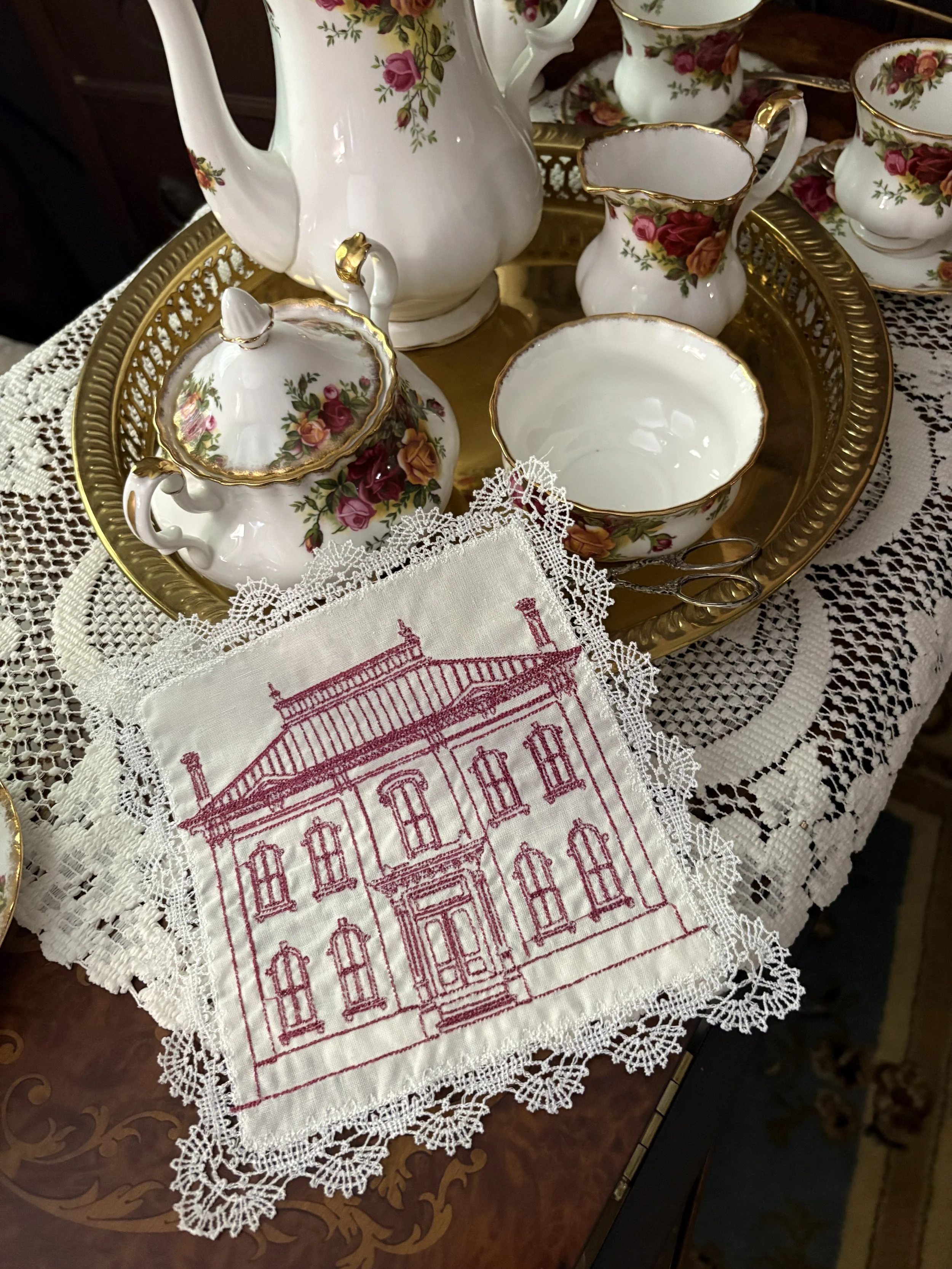 Handmade Victorian manor lace handkerchief with cranberry redwork embroidery displayed beside rose china tea service.
